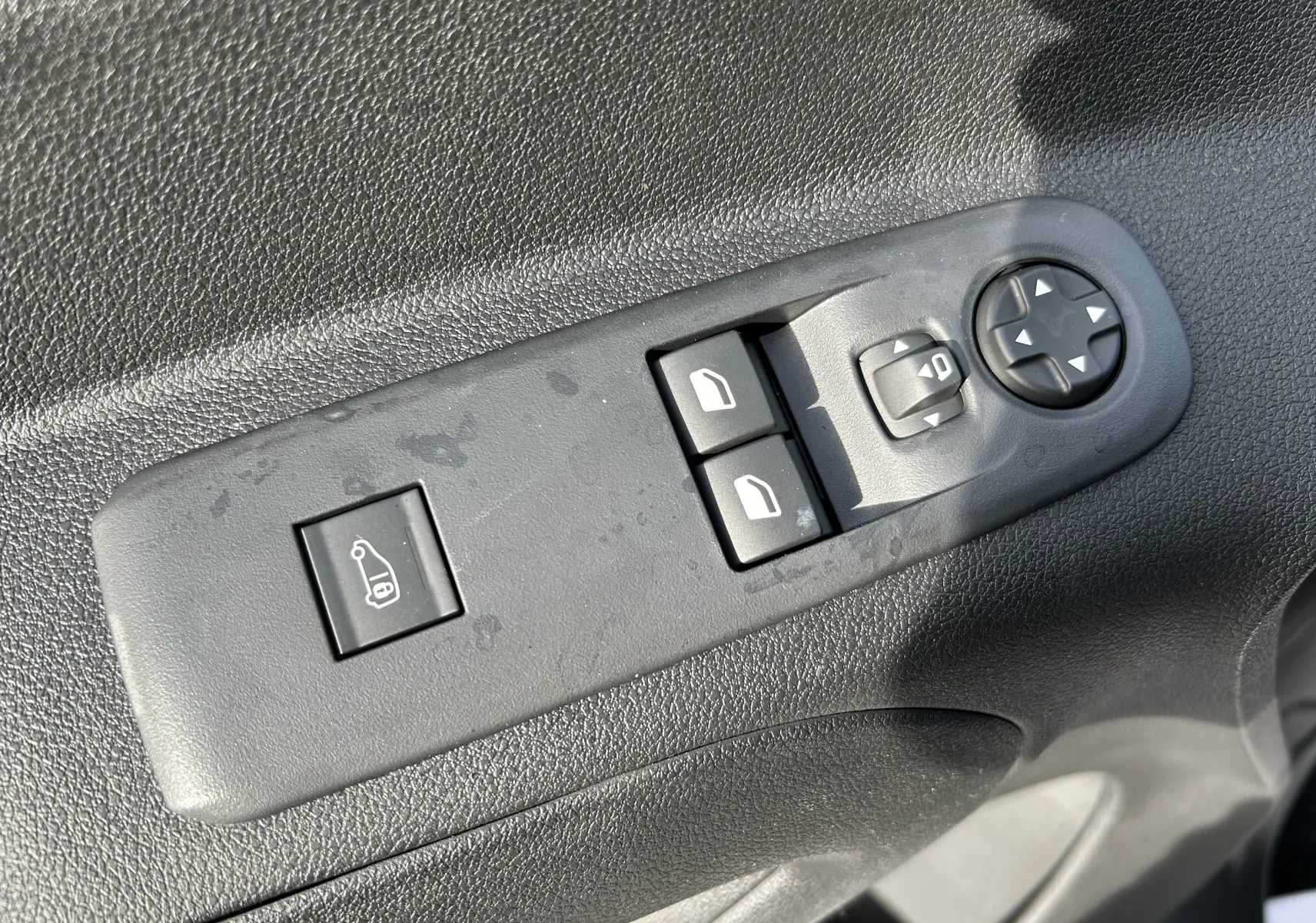 Panneau de commandes des vitres et rétroviseurs côté conducteur du Peugeot Partner Fourgon blanc, intérieur noir.