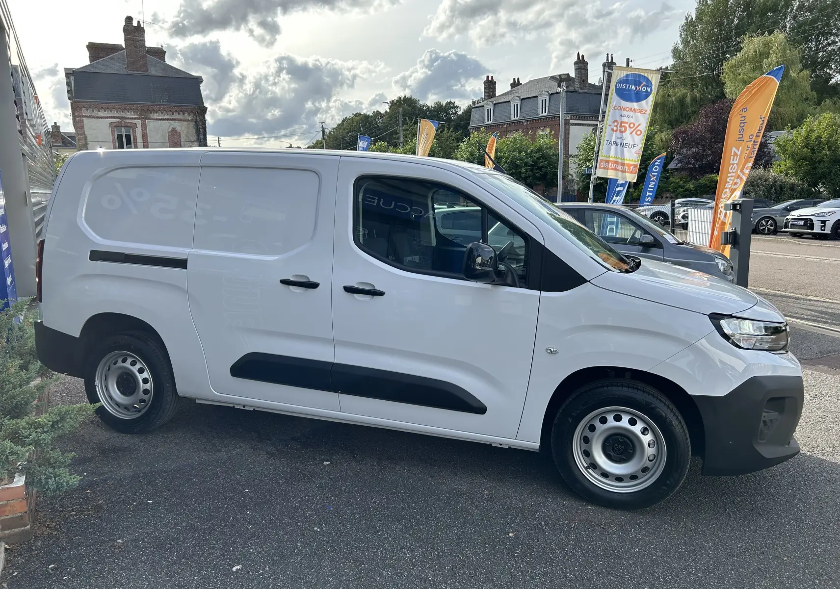 Profil côté droit d'un Peugeot Partner Fourgon blanc 2025 avec protections noires et jantes acier en extérieur urbain.