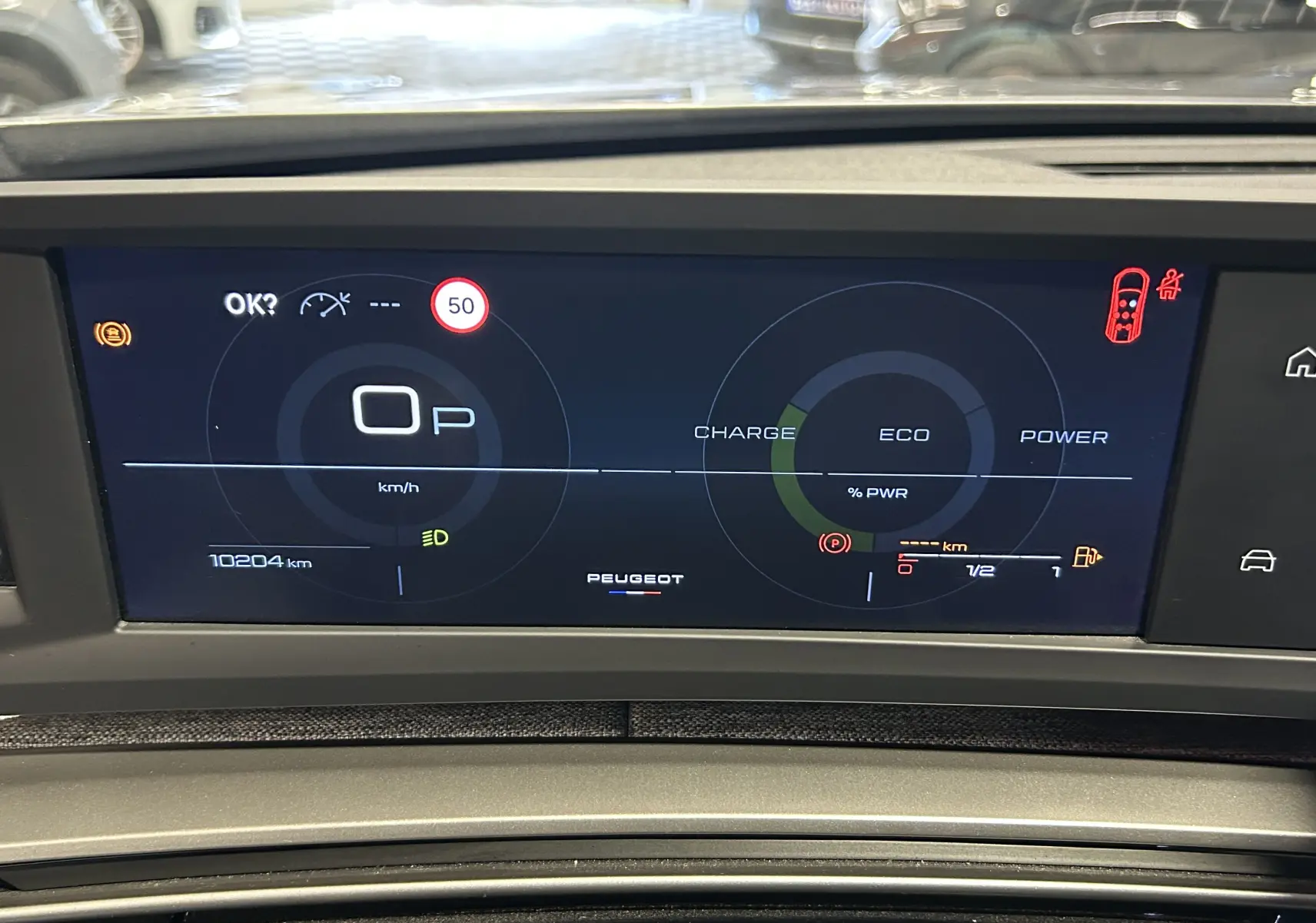 Affichage numérique du tableau de bord du Peugeot 5008 hybride gris Artense, montrant la vitesse à 0 km/h et l'état de charge.