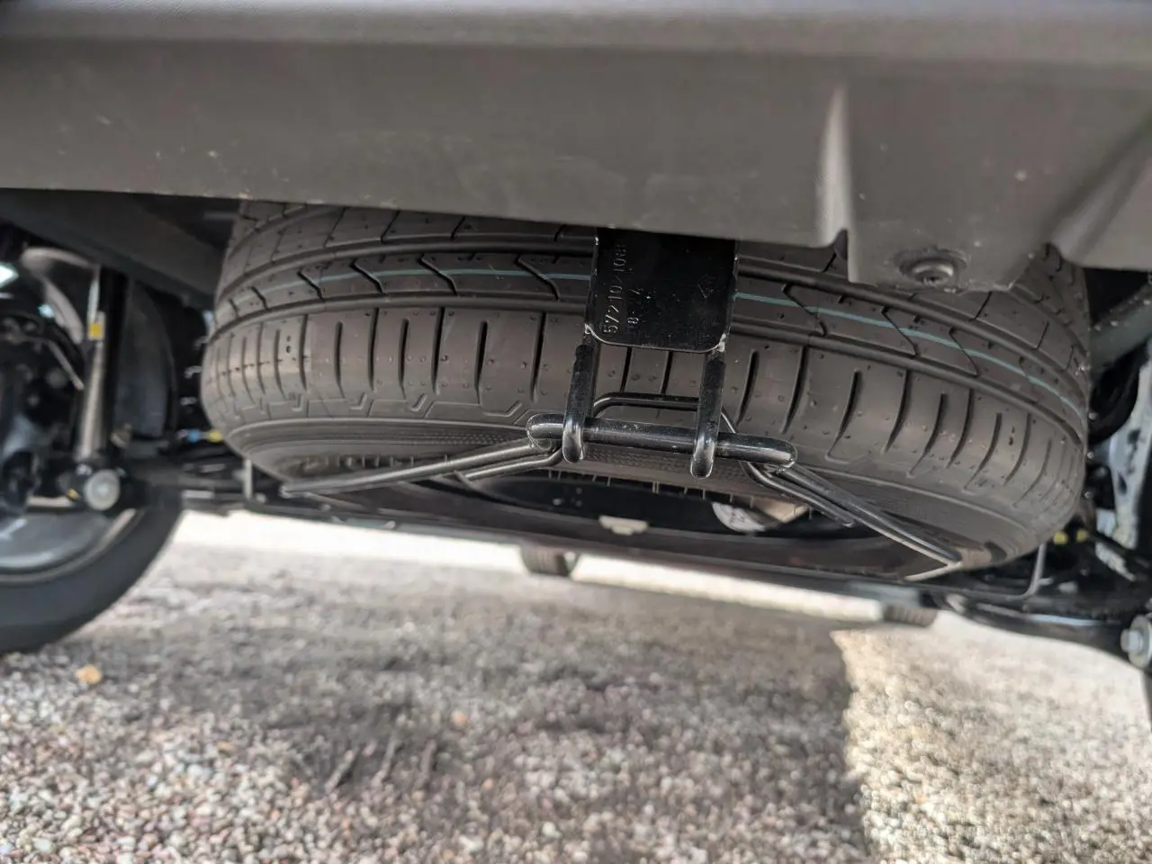 Gros plan sous le Dacia Jogger montrant la roue de secours suspendue sous le châssis, pneu noir visible.