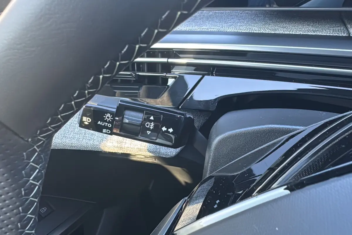 Détail du commodo d'éclairage à gauche du volant cuir dans l'habitacle du Peugeot 3008 gris titane 2025.