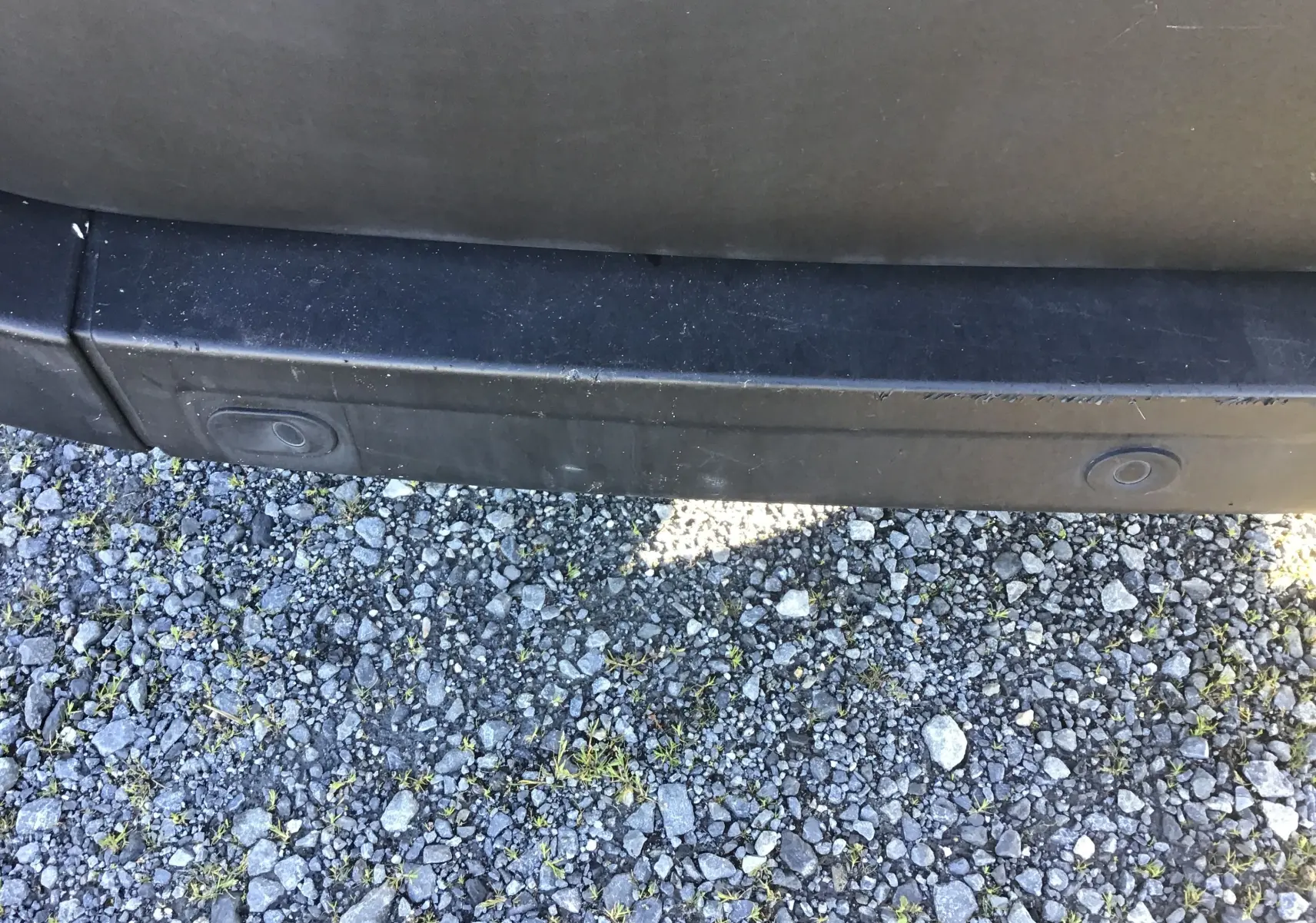 Gros plan sur le pare-chocs arrière noir du Renault Master blanc, montrant les capteurs de recul sur un sol gravillonné.