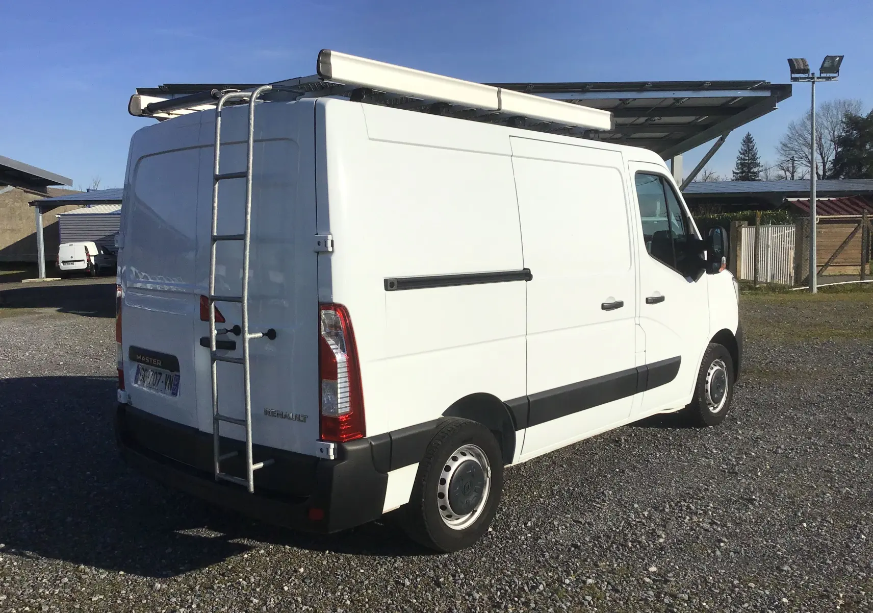 Vue 3/4 arrière droite d’un Renault Master blanc 2022 avec galerie, échelle arrière et porte latérale fermée.