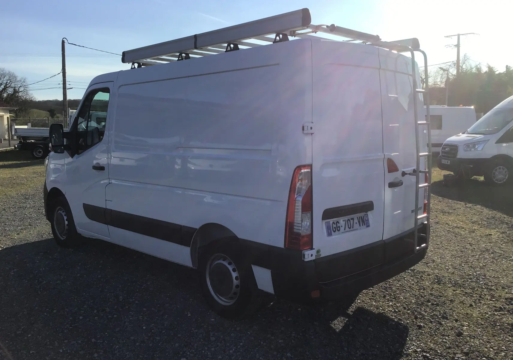 Vue 3/4 arrière droite d’un Renault Master blanc 2022 avec galerie de toit et échelle arrière.