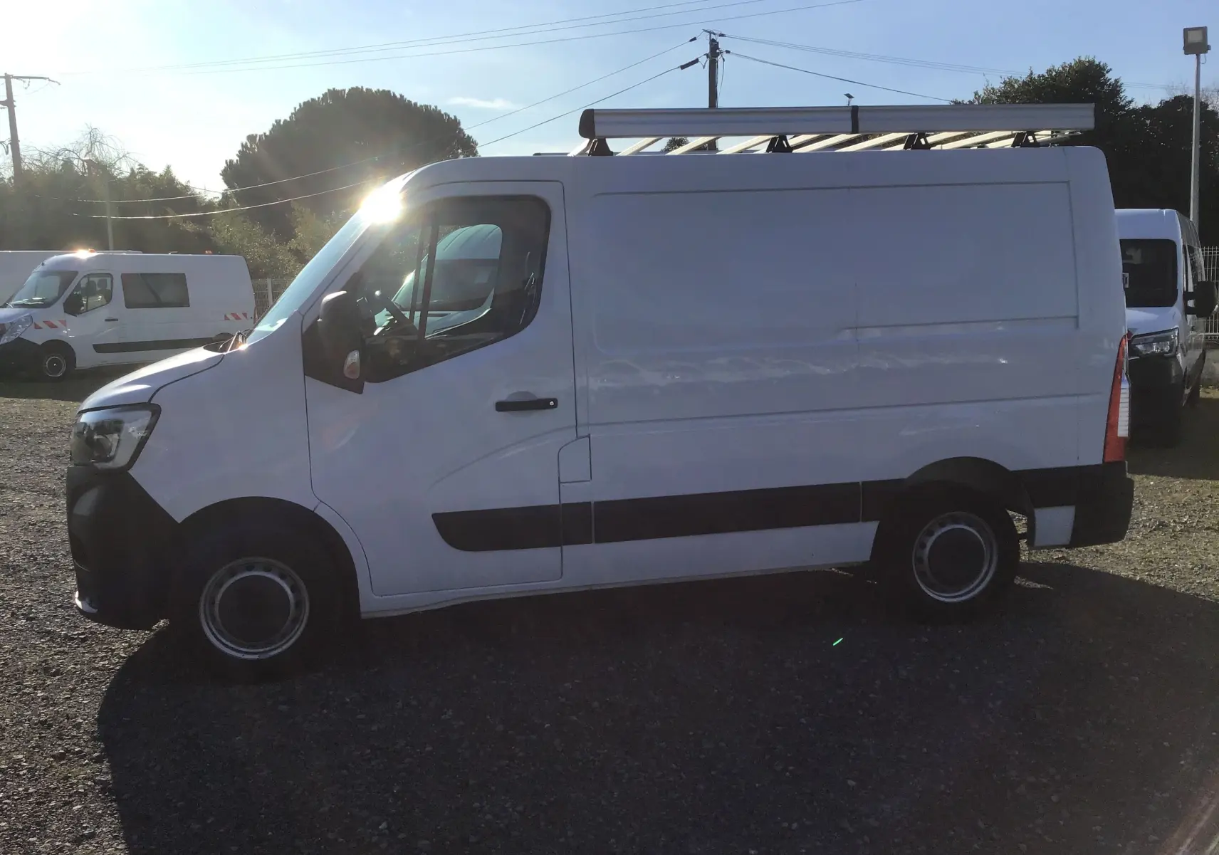 Vue latérale gauche d’un Renault Master blanc 2022 avec galerie de toit et bande noire sur le bas de caisse.