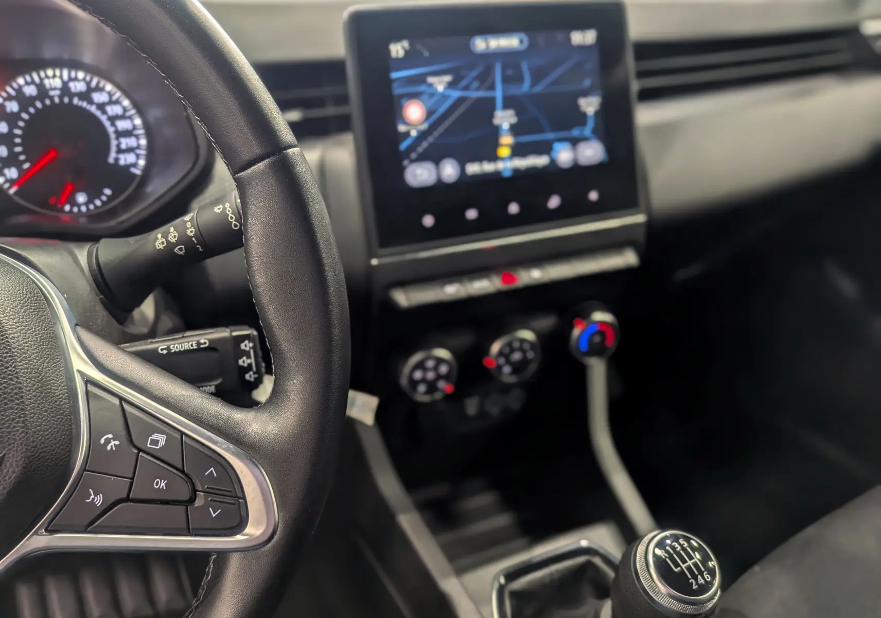 Vue intérieure centrée sur le volant et la console centrale avec levier de vitesse manuel de la Renault Clio V gris platine.