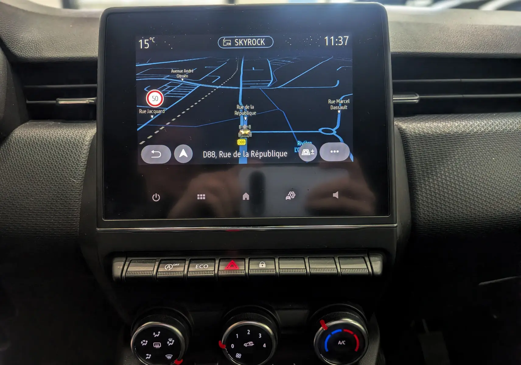 Écran tactile central avec navigation GPS et commandes de climatisation dans Renault Clio V TCe 90 Gris Platine, vue intérieure frontale.