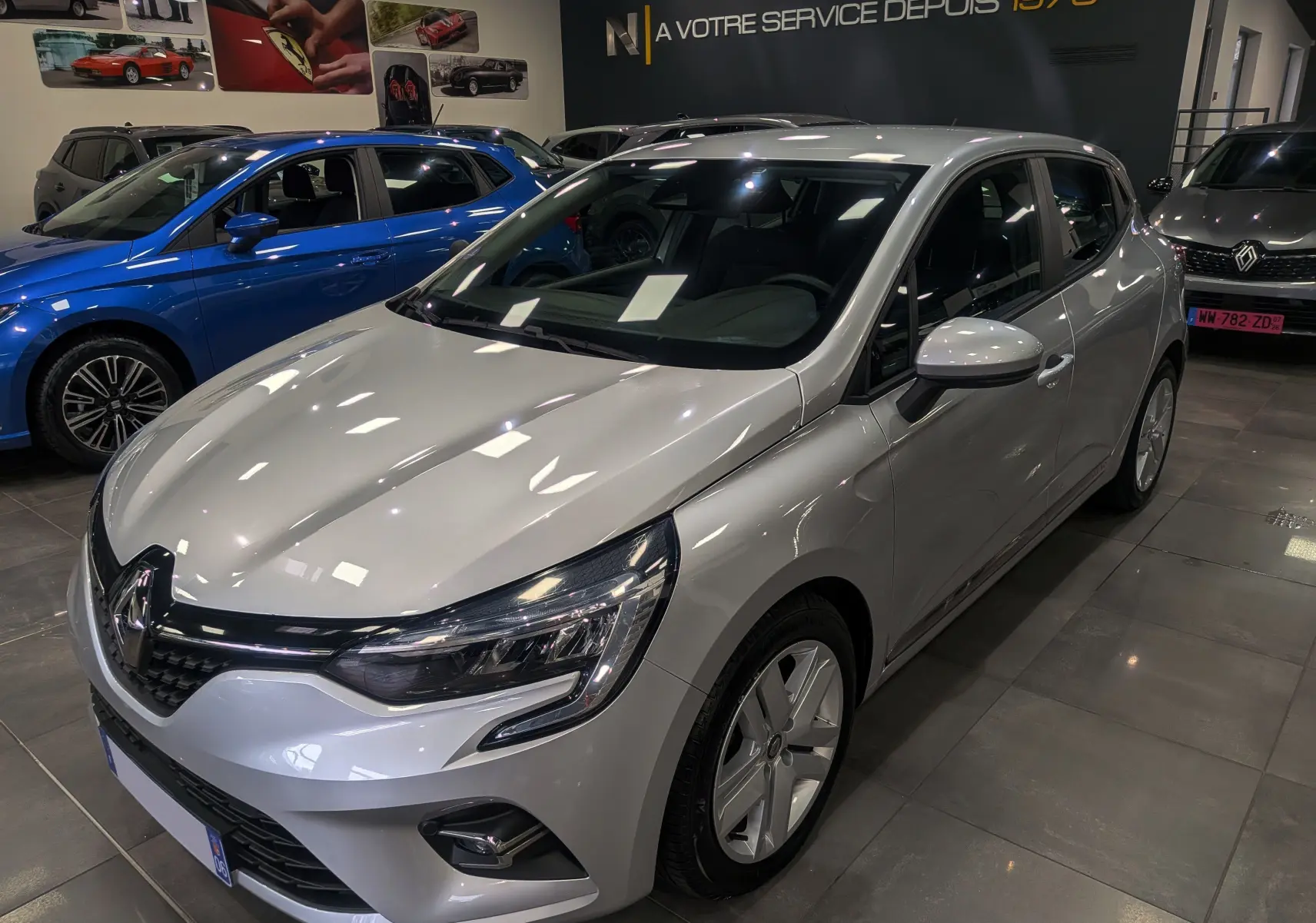 Renault Clio V gris platine vue 3/4 avant droit en showroom, avec phares LED et jantes alliage visibles.