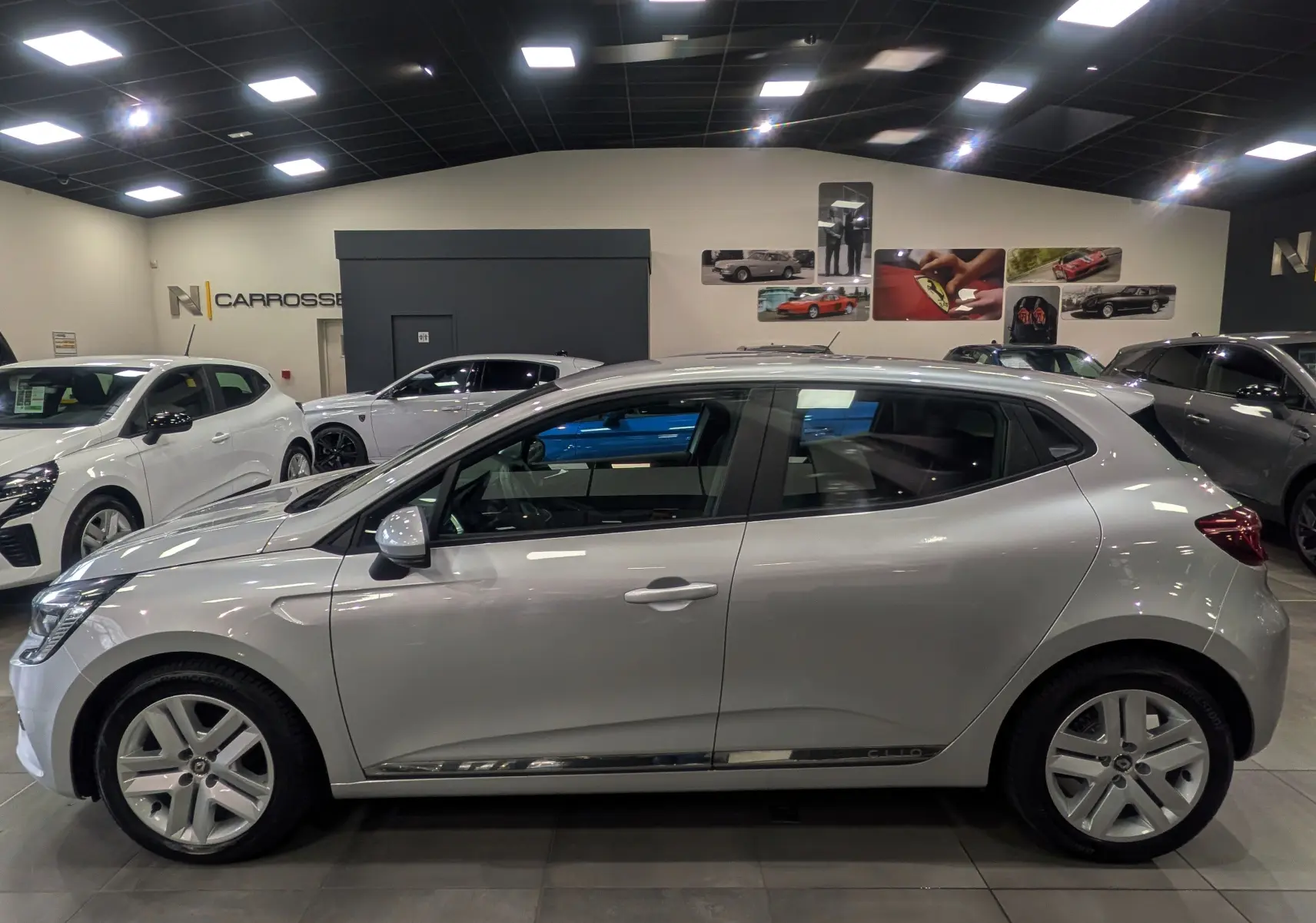 Profil côté gauche d'une Renault Clio V gris platine 2021 en intérieur, avec jantes alliage et vitres teintées.