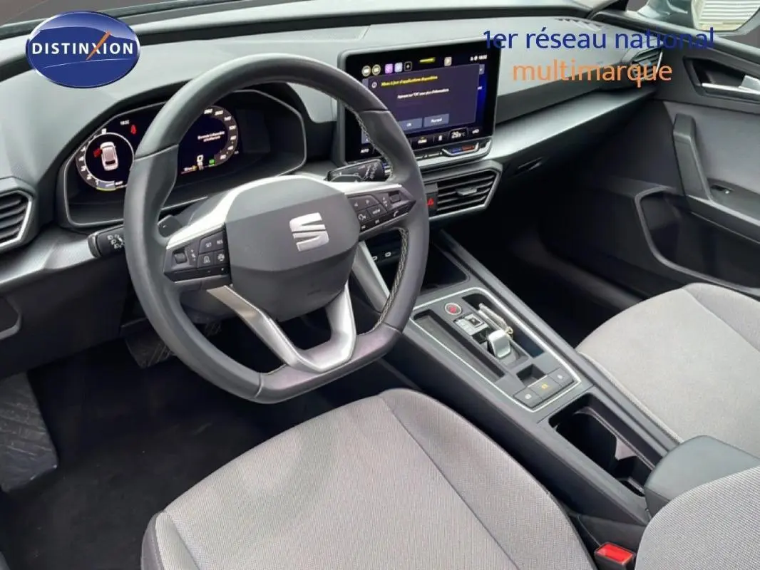 Vue intérieure côté conducteur du SEAT Leon ST IV 2025, volant cuir multifonctions et écran tactile central visible.