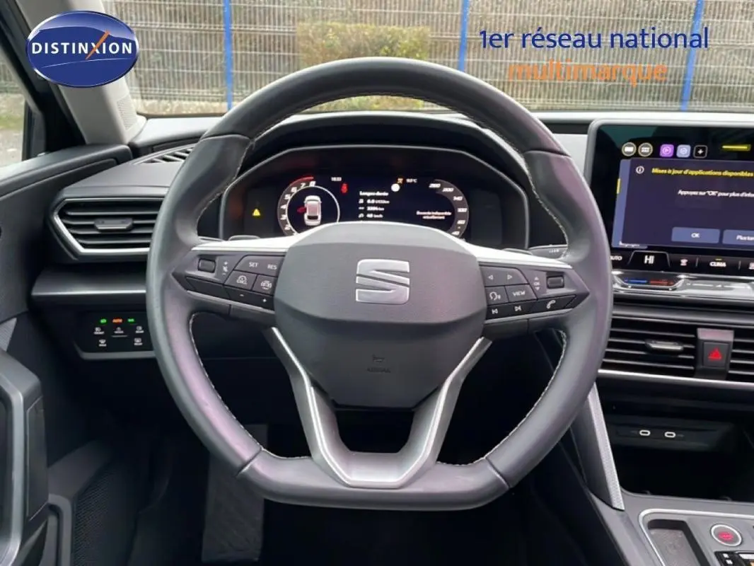 Vue intérieure centrée sur le volant cuir multifonctions d’une SEAT Leon ST IV 2025 avec écran tactile et tableau de bord numérique.