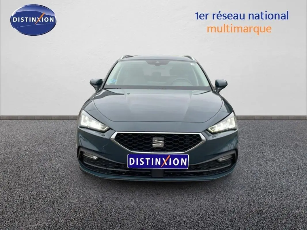 Vue frontale d'une SEAT Leon ST IV bleu avec phares allumés et barres de toit visibles sur fond neutre.