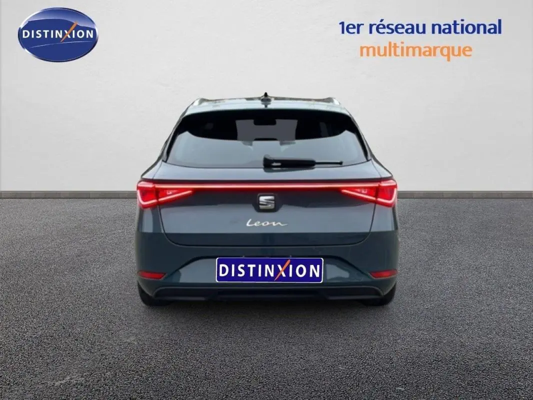 Vue arrière d'une SEAT Leon ST IV bleu avec feux arrière allumés et barres de toit visibles sur fond neutre.