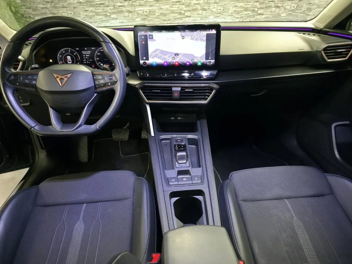 Vue intérieure avant de la CUPRA Leon Sportstourer 2024, volant cuir avec logo cuivre et écran tactile central lumineux.