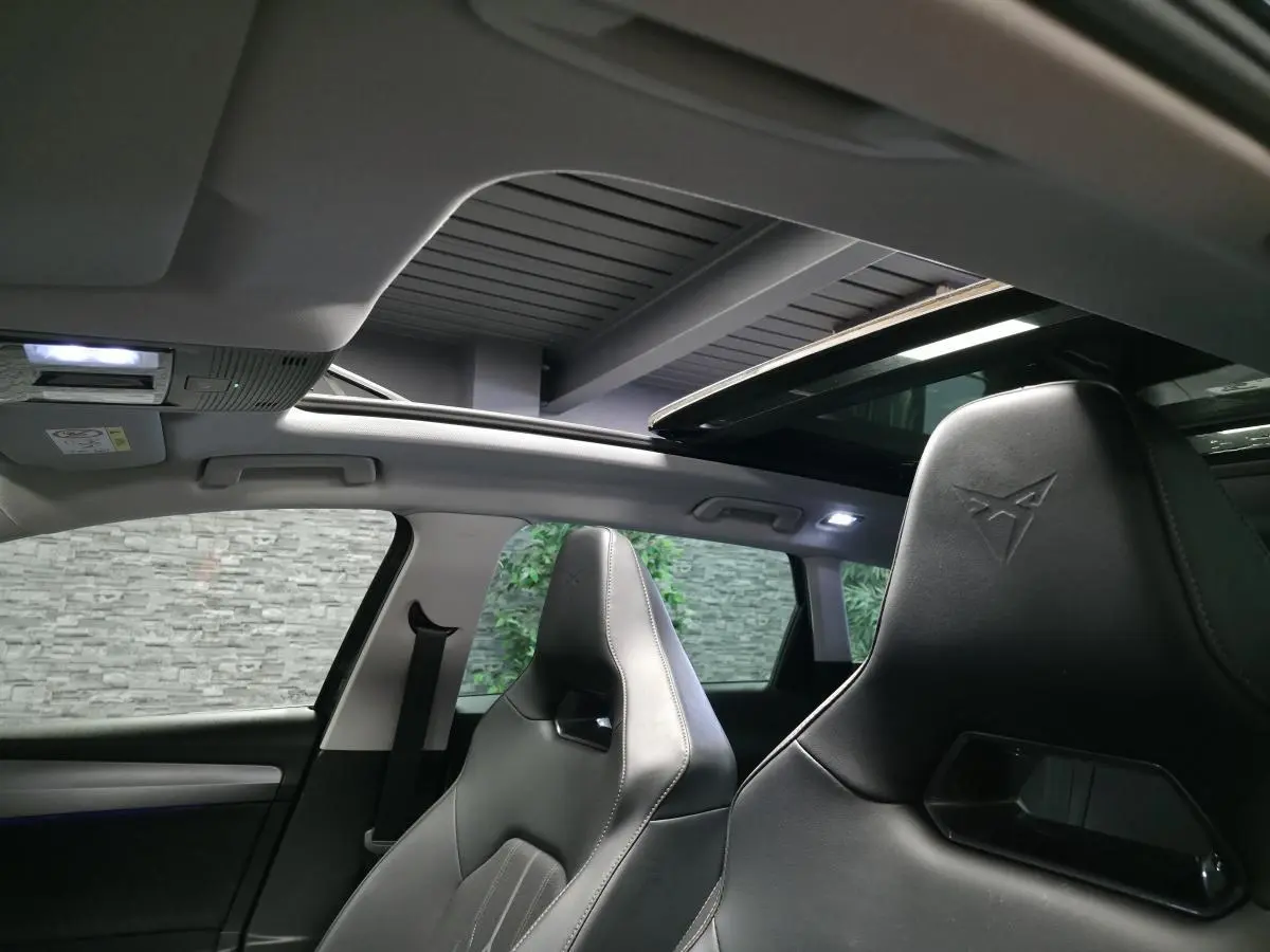 Vue intérieure avant du CUPRA Leon Sportstourer gris, sièges baquets noirs avec logo embossé et toit ouvrant panoramique.