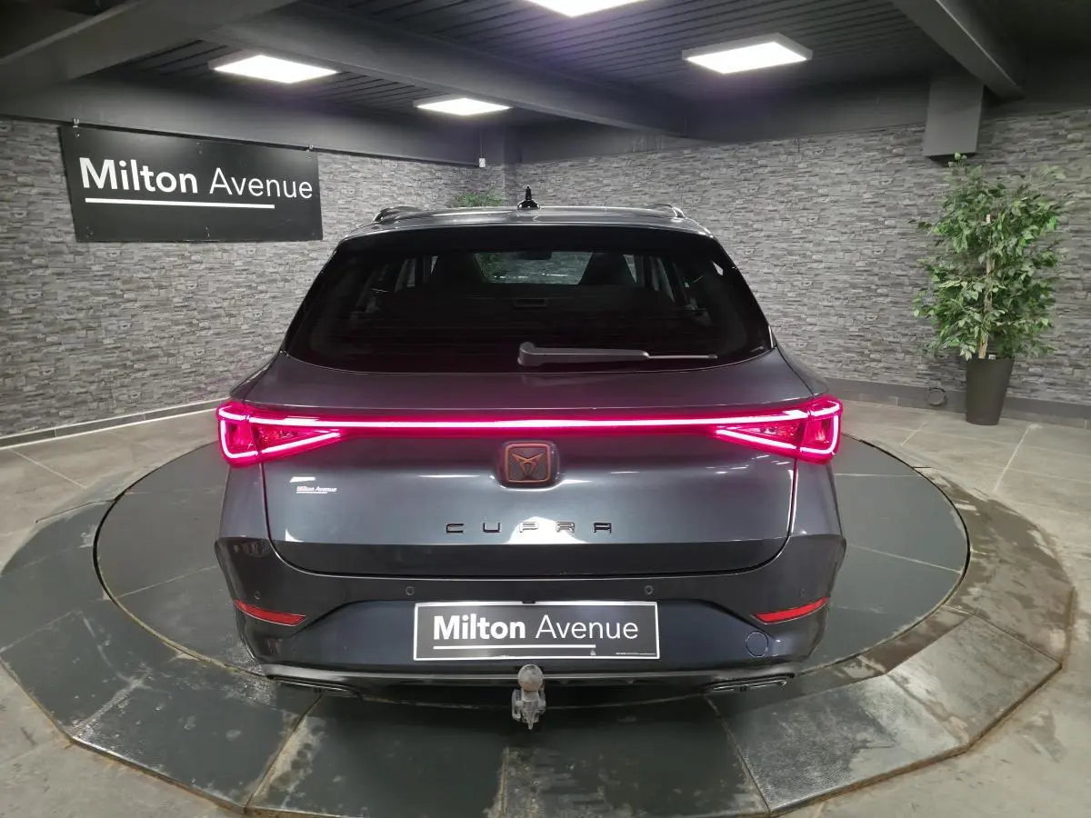 Vue arrière d'une CUPRA Leon Sportstourer gris magnétique avec feux LED allumés et crochet d'attelage escamotable visible.