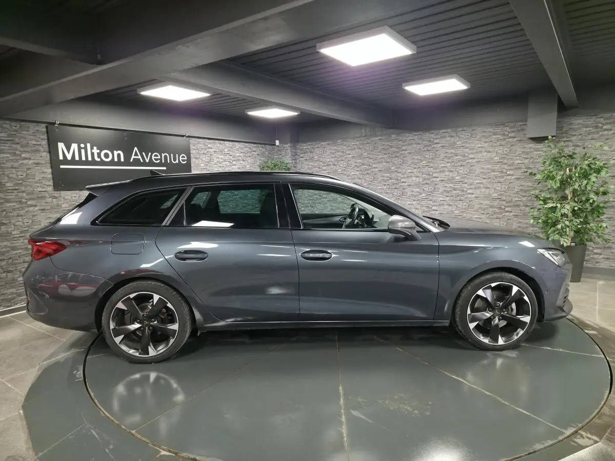 Vue de profil côté gauche d'une CUPRA Leon Sportstourer gris magnétique avec jantes alliage 18 pouces dans un showroom.
