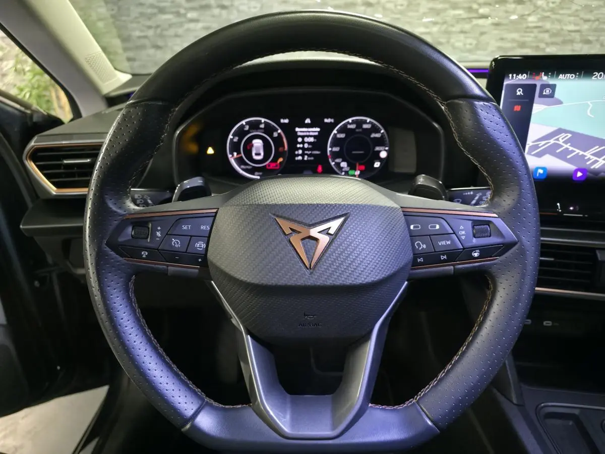 Vue rapprochée du volant cuir noir à surpiqûres copper de la CUPRA Leon 2024 avec tableau de bord digital et écran tactile.