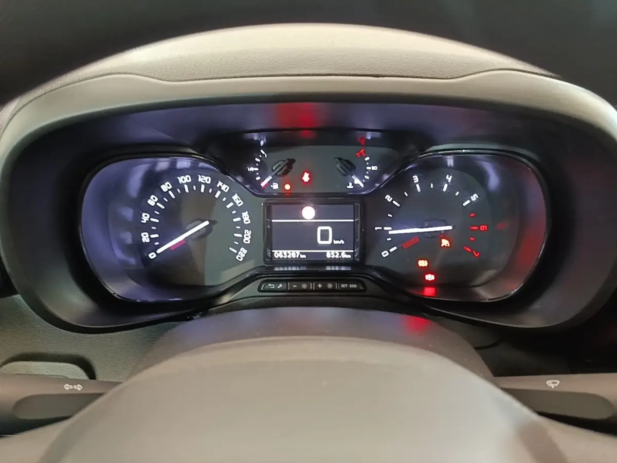 Vue rapprochée du tableau de bord digital du Citroën Berlingo blanc, affichant 0 km/h et divers voyants allumés.