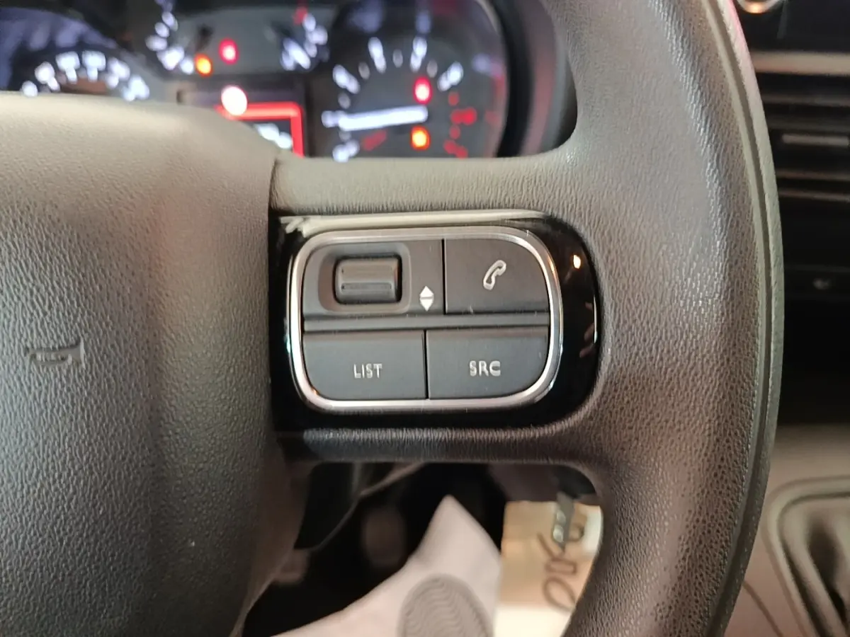 Gros plan sur les commandes gauche du volant noir du Citroën Berlingo 2020 avec tableau de bord flou en arrière-plan.