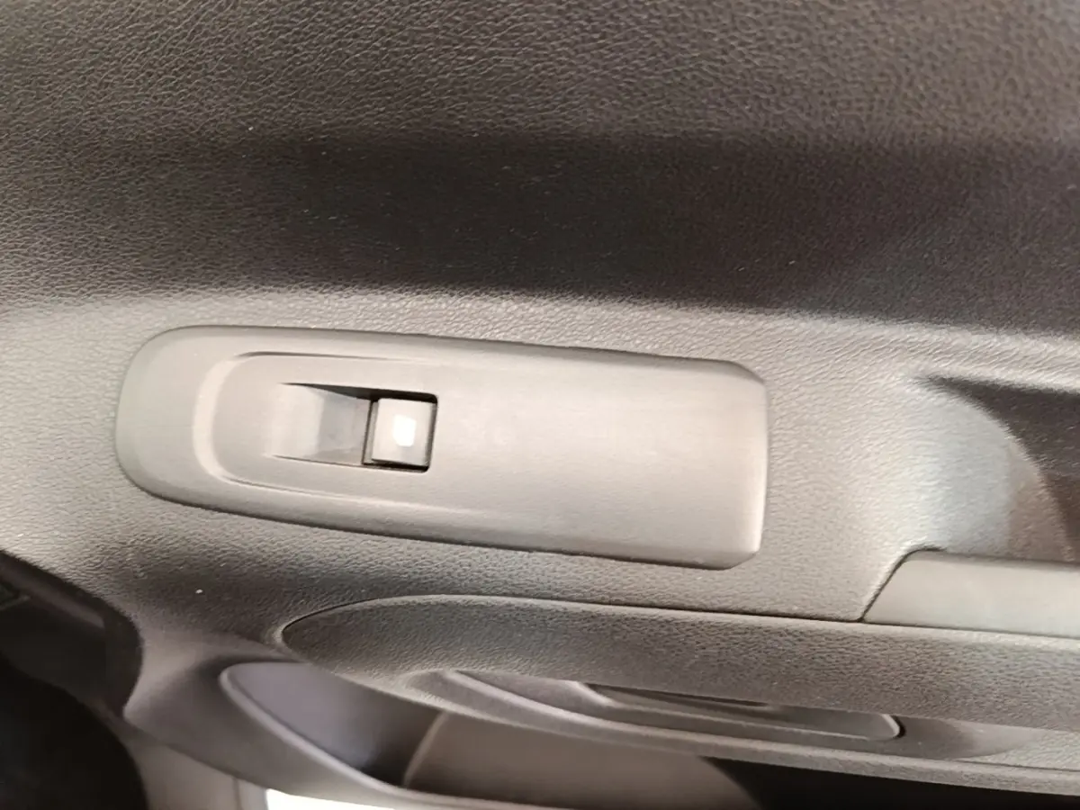 Gros plan sur le bouton de commande de la vitre électrique côté conducteur dans l'intérieur noir du Citroën Berlingo blanc.