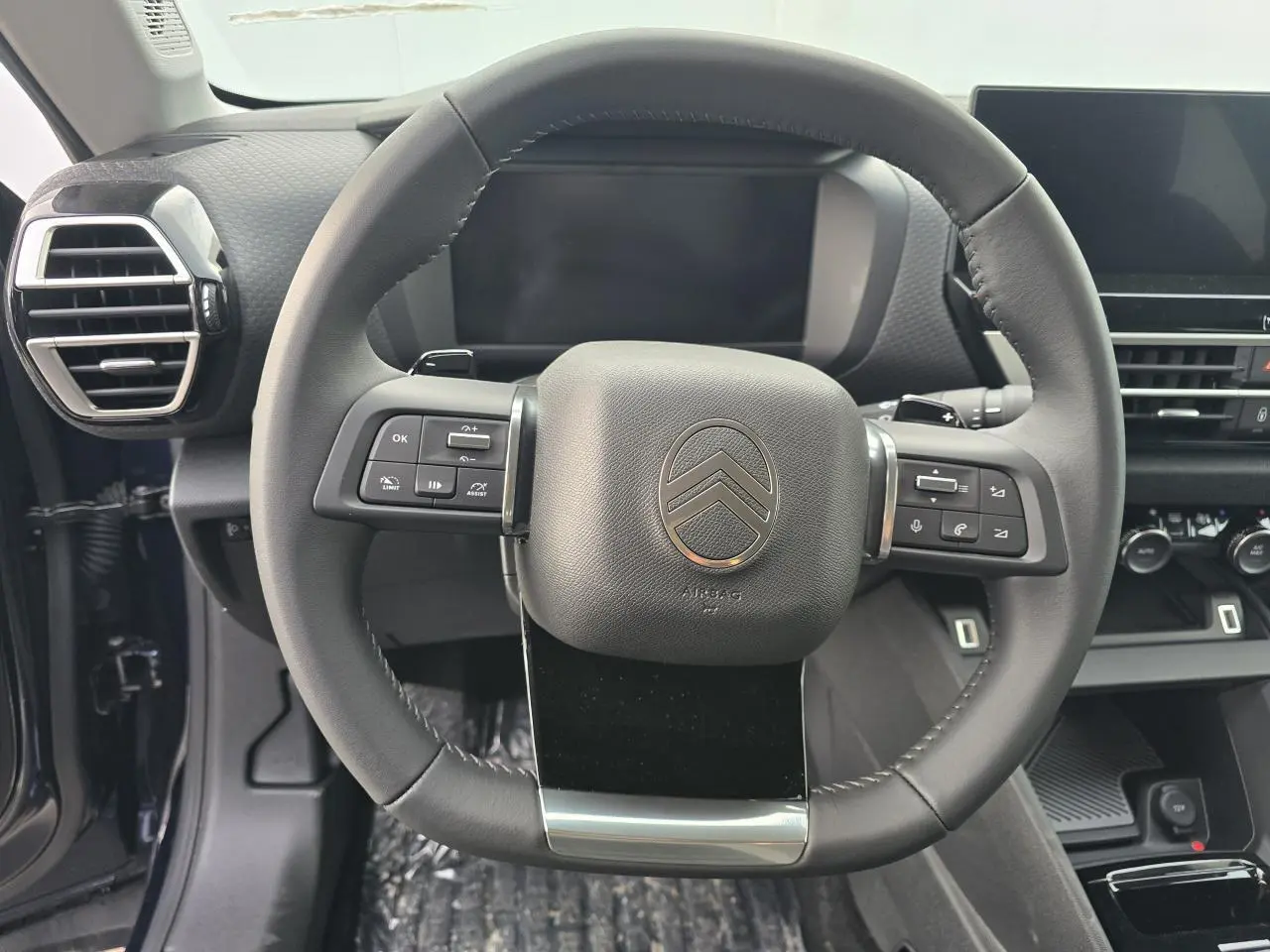 Volant cuir noir Citroën C4 2025 vu de face avec commandes intégrées et tableau de bord numérique en arrière-plan.