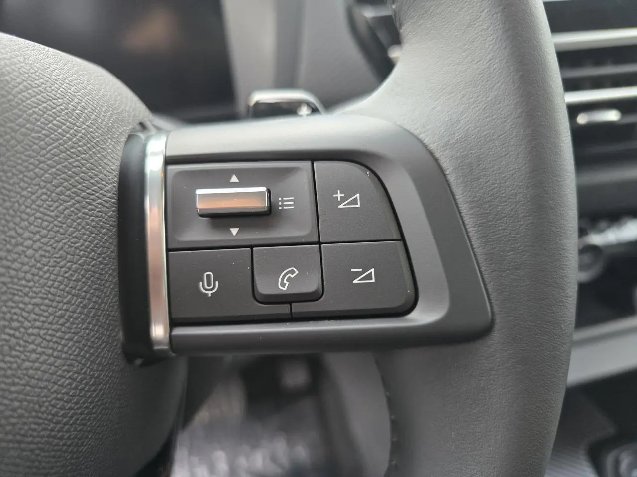 Gros plan sur les commandes vocales et téléphone au volant cuir noir de la Citroën C4 III hybride 2025.