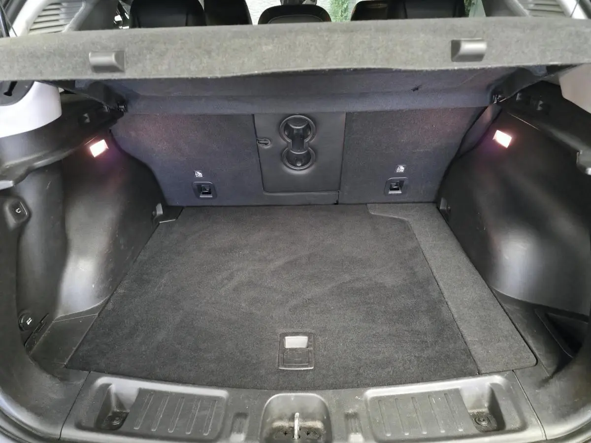 Coffre spacieux du Jeep Compass 2022 hybride rechargeable, vue de l'intérieur avec tapis noir et éclairage latéral.