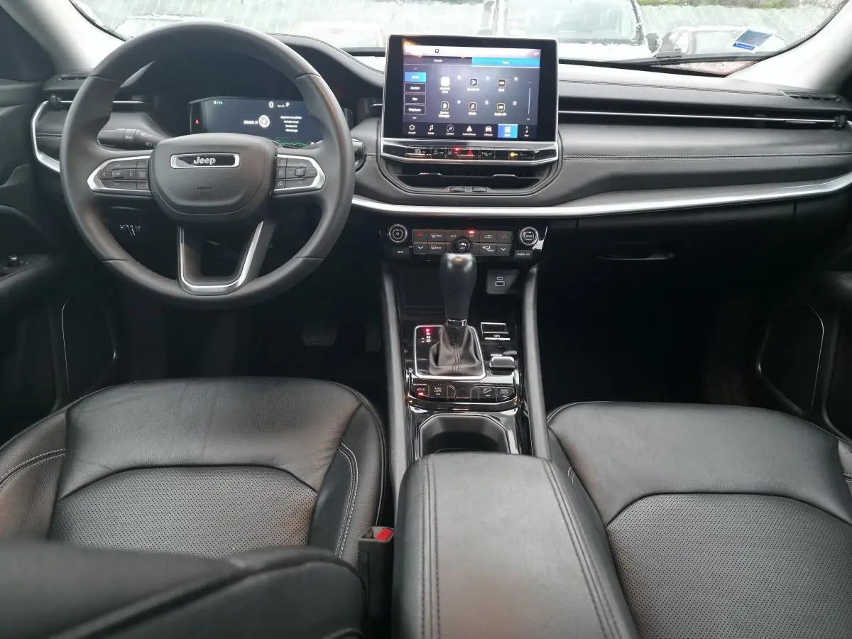 Intérieur du Jeep Compass 2022 en vue frontale, sièges cuir noirs et tableau de bord avec écran tactile central.