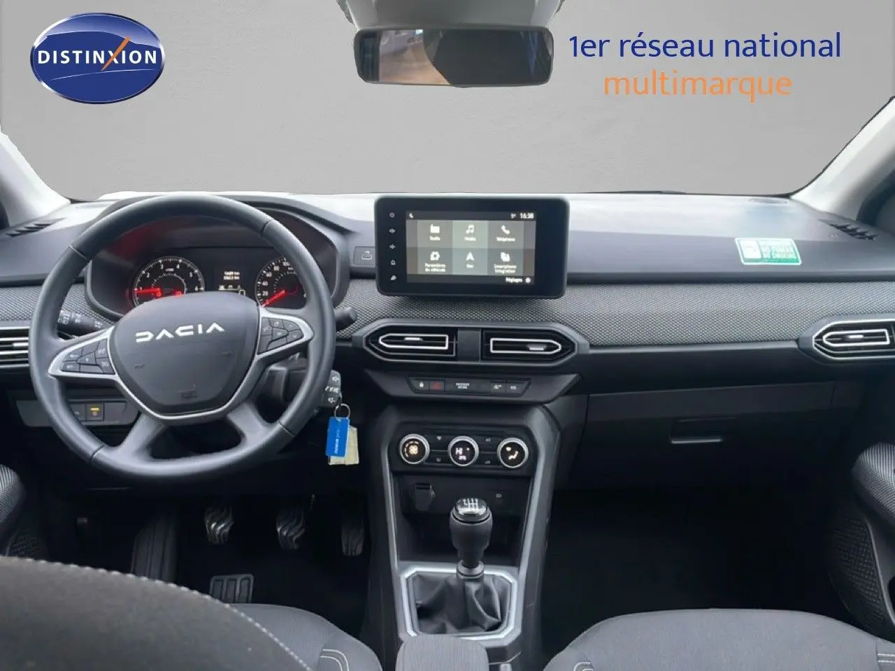 Vue intérieure avant du tableau de bord et volant noir du Dacia Jogger 2025, avec écran tactile central et levier de vitesses manuel.