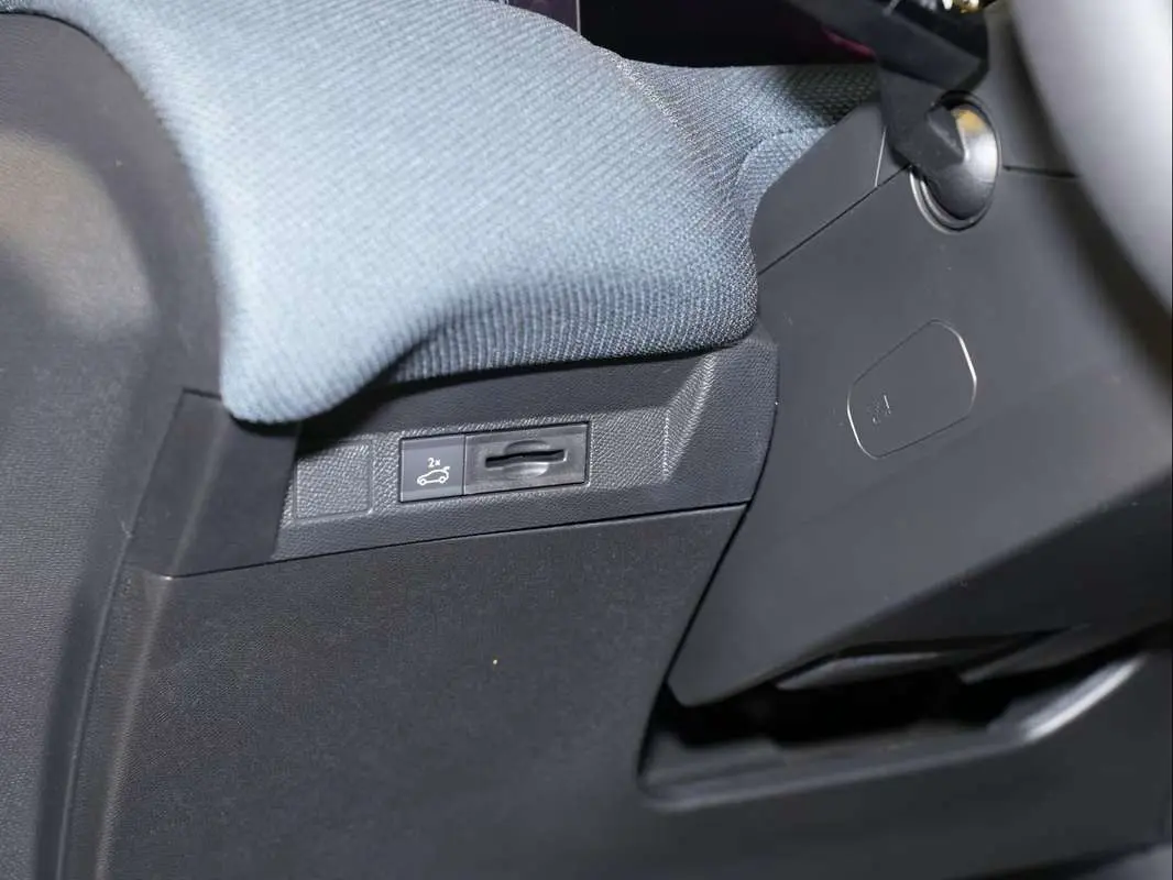 Gros plan sur le bouton d'ouverture du hayon sous le tableau de bord côté conducteur du Citroën C5 Aircross gris platinium.