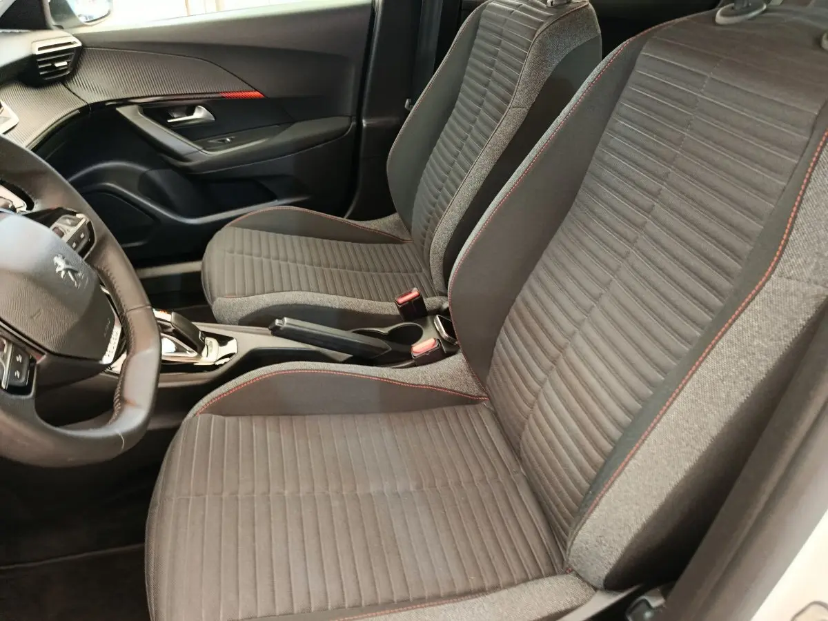 Vue intérieure côté conducteur du Peugeot 2008 blanc, sièges tissu gris avec surpiqûres rouges et volant cuir multifonctions.