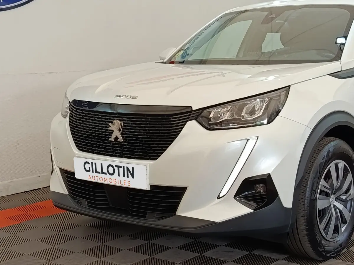 Vue 3/4 avant droit d’un Peugeot 2008 blanc avec calandre noire et feux LED verticaux allumés.