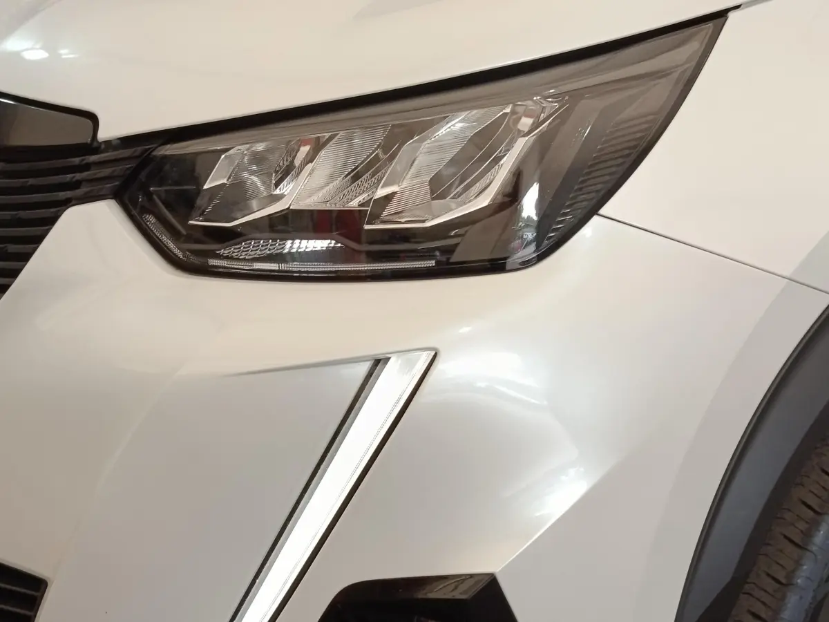 Gros plan sur le phare avant droit blanc du Peugeot 2008 avec signature lumineuse verticale LED.