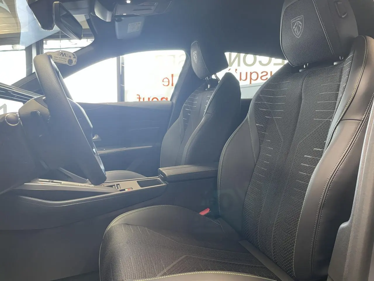 Vue intérieure côté gauche des sièges avant noirs avec surpiqûres vert Adamite et logo Peugeot brodé sur appuie-tête.