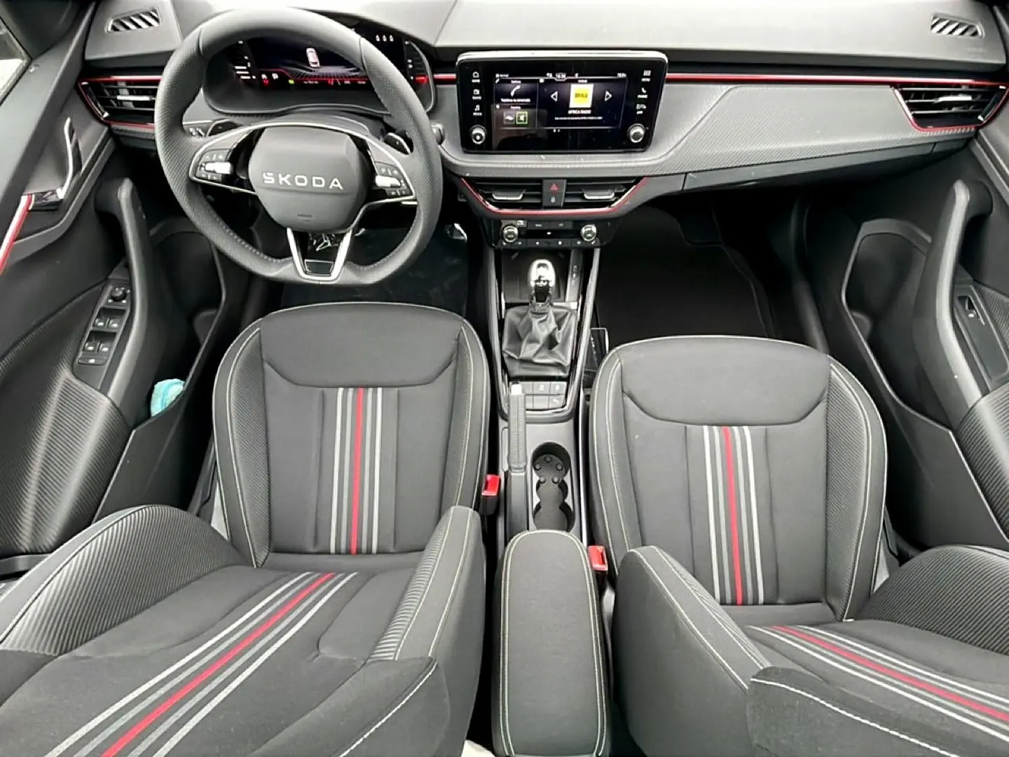 Vue intérieure frontale du Skoda Kamiq 2026 noir, sièges sport Monte Carlo avec bandes rouges et tableau de bord moderne.