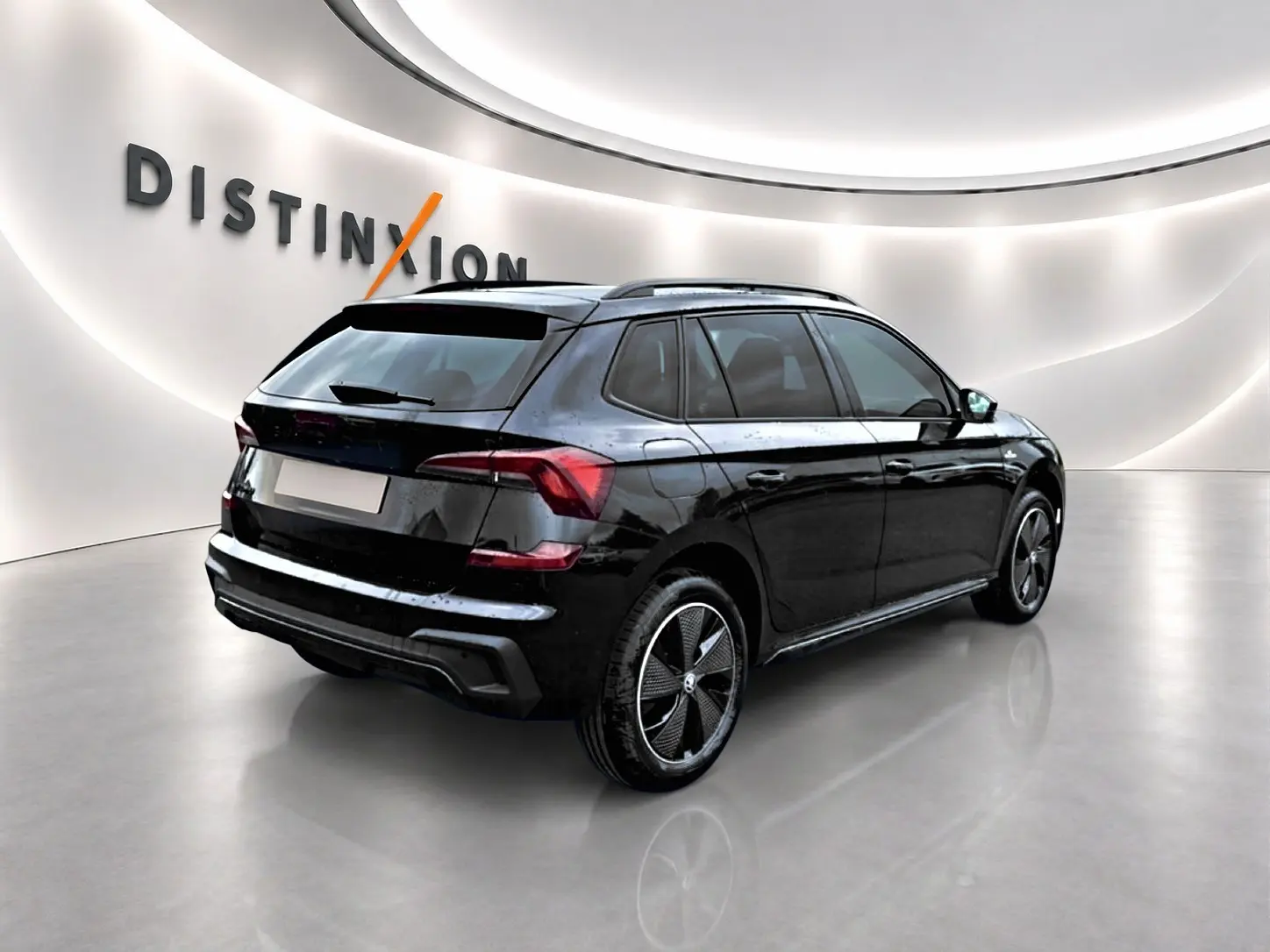 Vue 3/4 arrière droite d'un Skoda Kamiq noir avec jantes alu noires et toit panoramique en showroom lumineux.