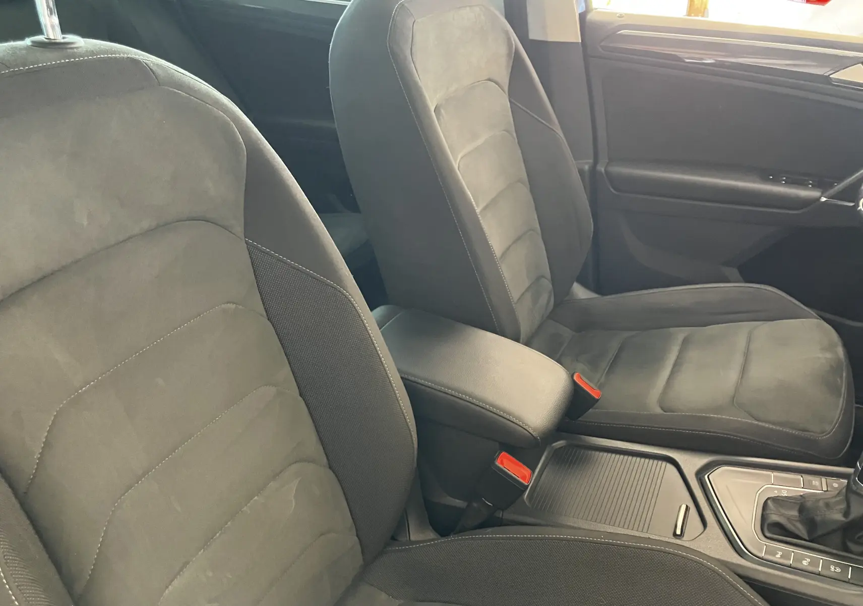 Vue intérieure des sièges avant en tissu noir du Volkswagen Tiguan 2017, avec accoudoir central et console de boîte automatique visible.