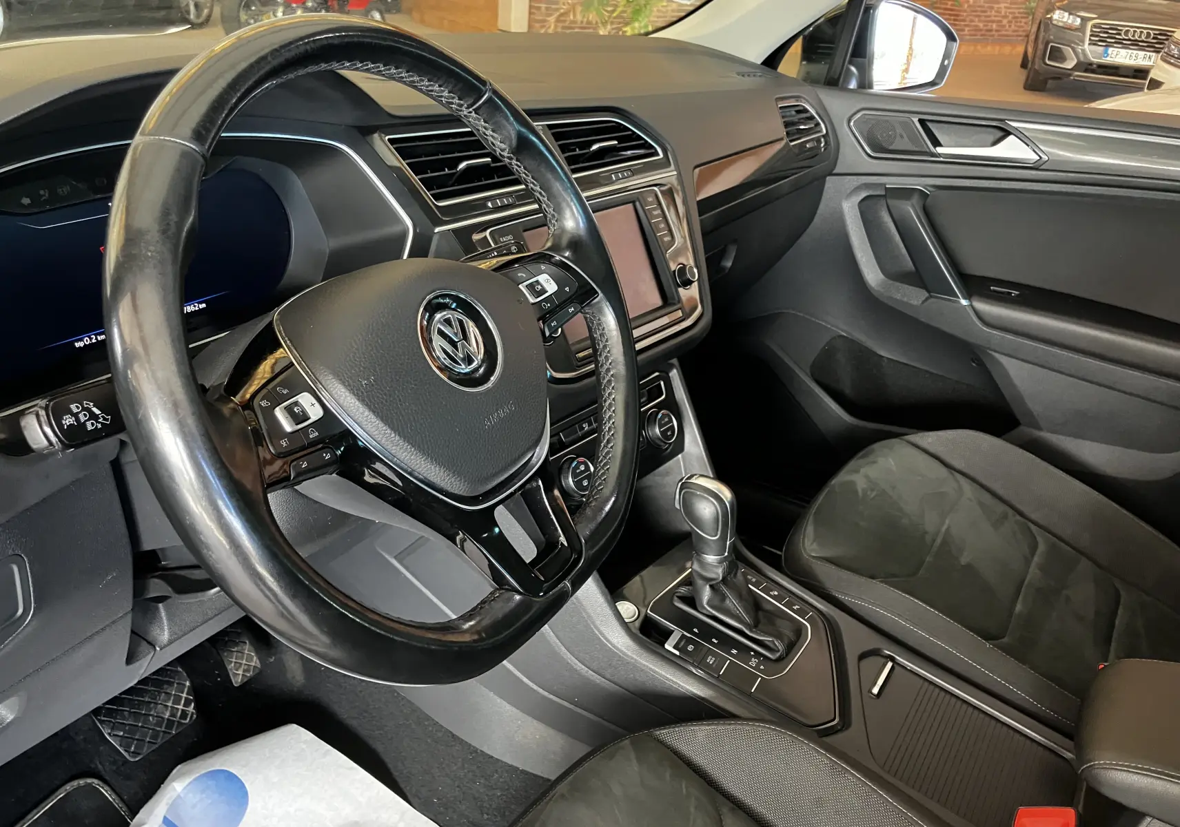 Intérieur noir du Volkswagen Tiguan 2017, vue côté conducteur sur volant cuir, console centrale et siège avant droit.