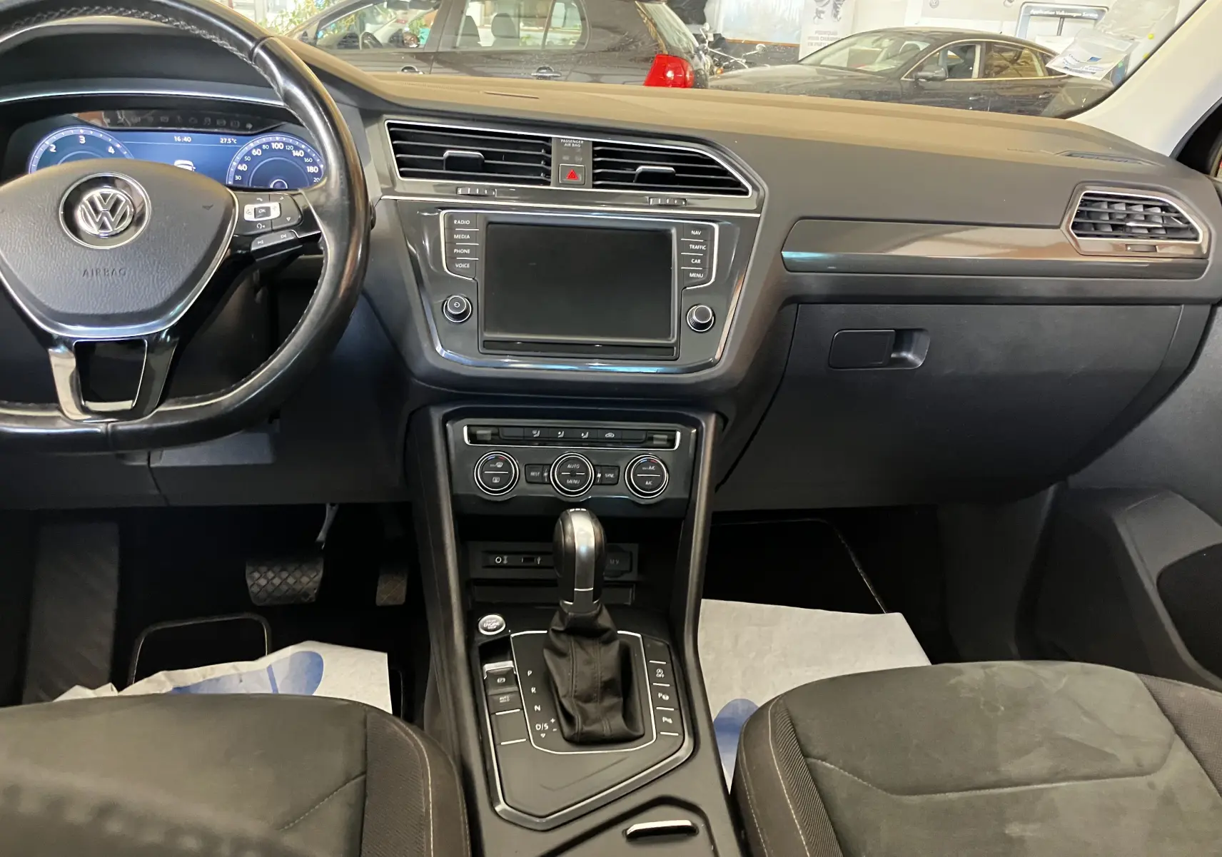 Vue intérieure du tableau de bord et console centrale du Volkswagen Tiguan noir 2017 avec volant multifonction et écran tactile éteint.