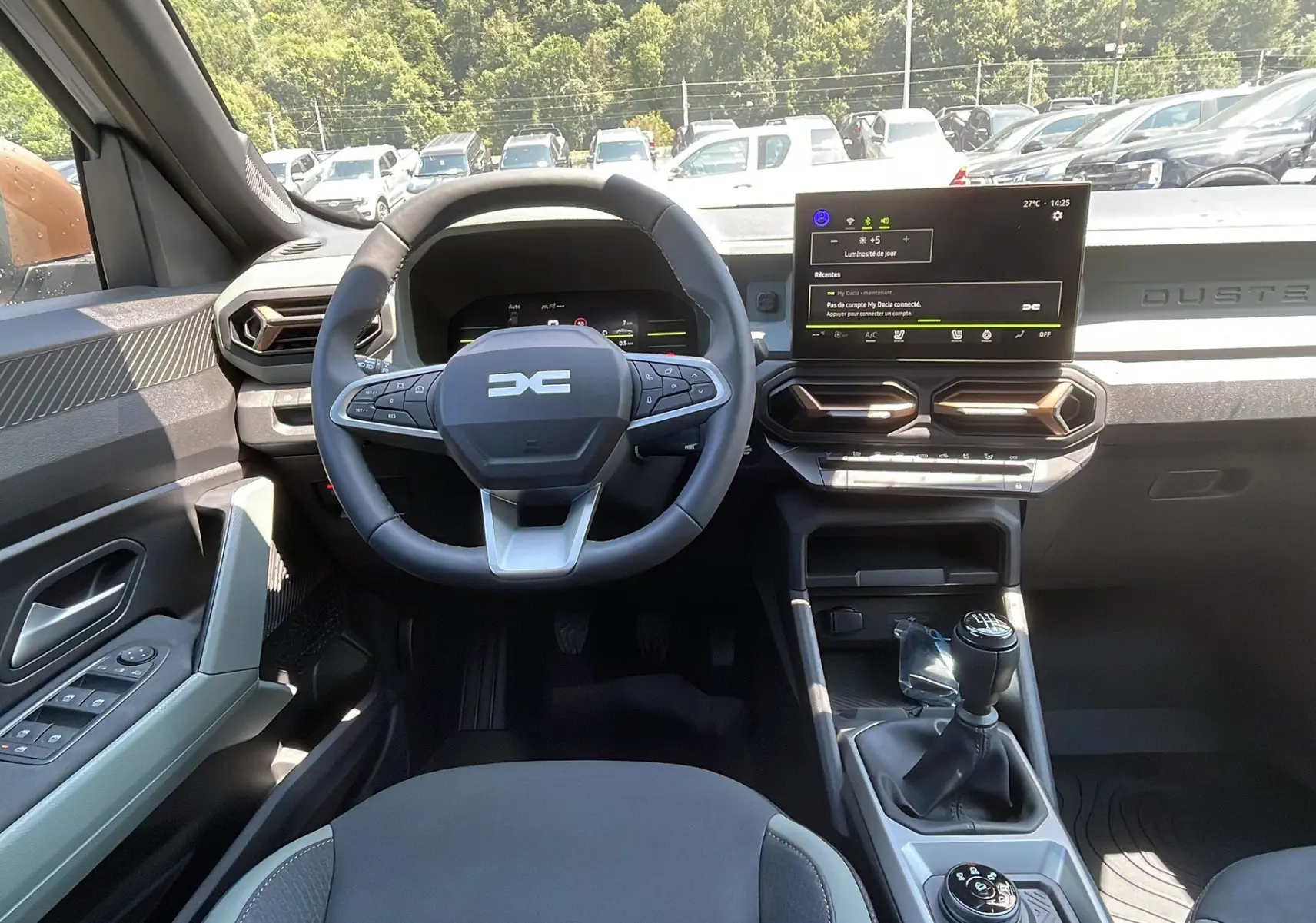 Intérieur du Dacia Duster 2025 blanc, vue du poste de conduite avec volant multifonction et boîte manuelle visible.