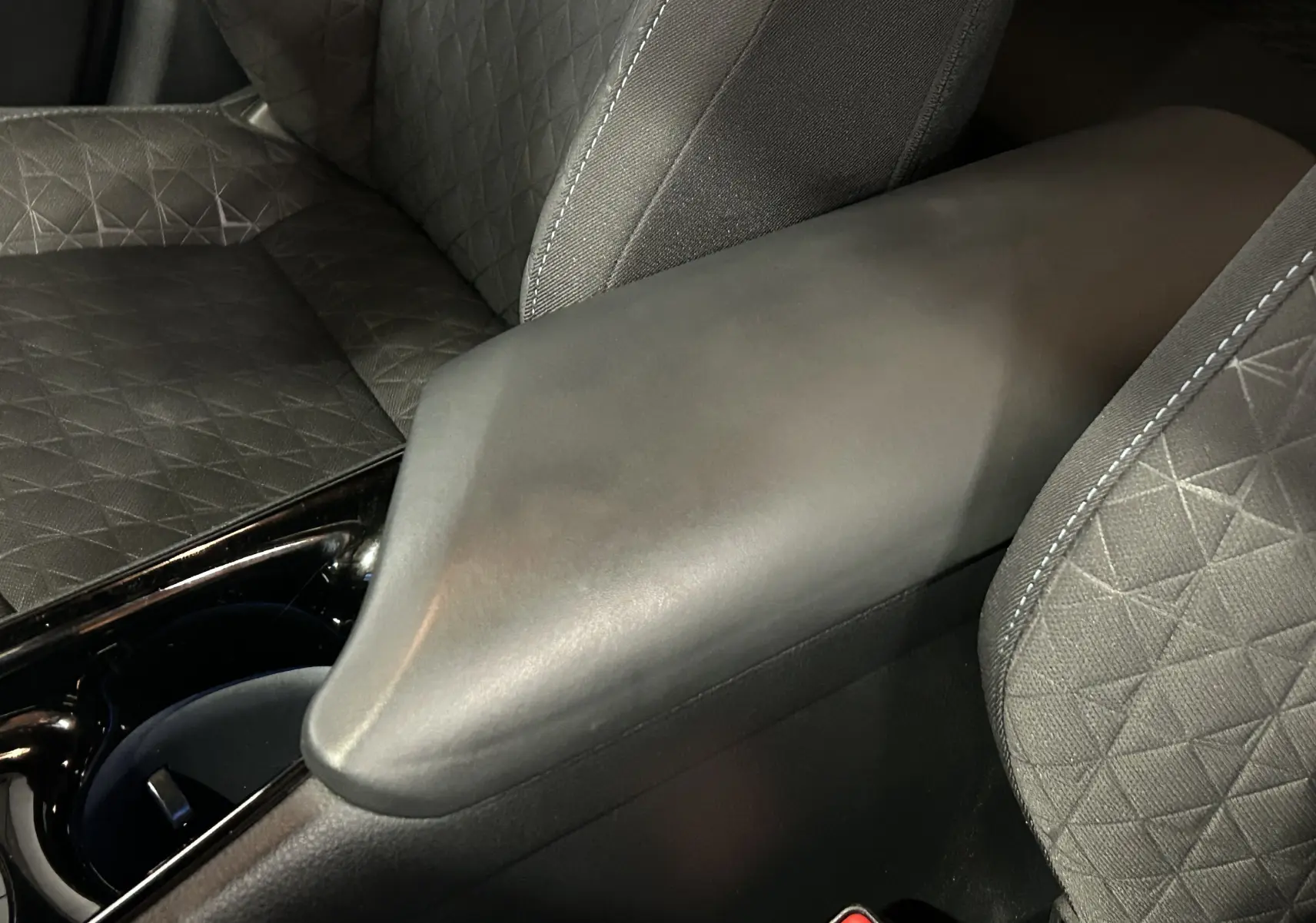 Détail de l'accoudoir central noir mat et des sièges en tissu gris à motifs géométriques dans un Toyota C-HR Hybride 2021.