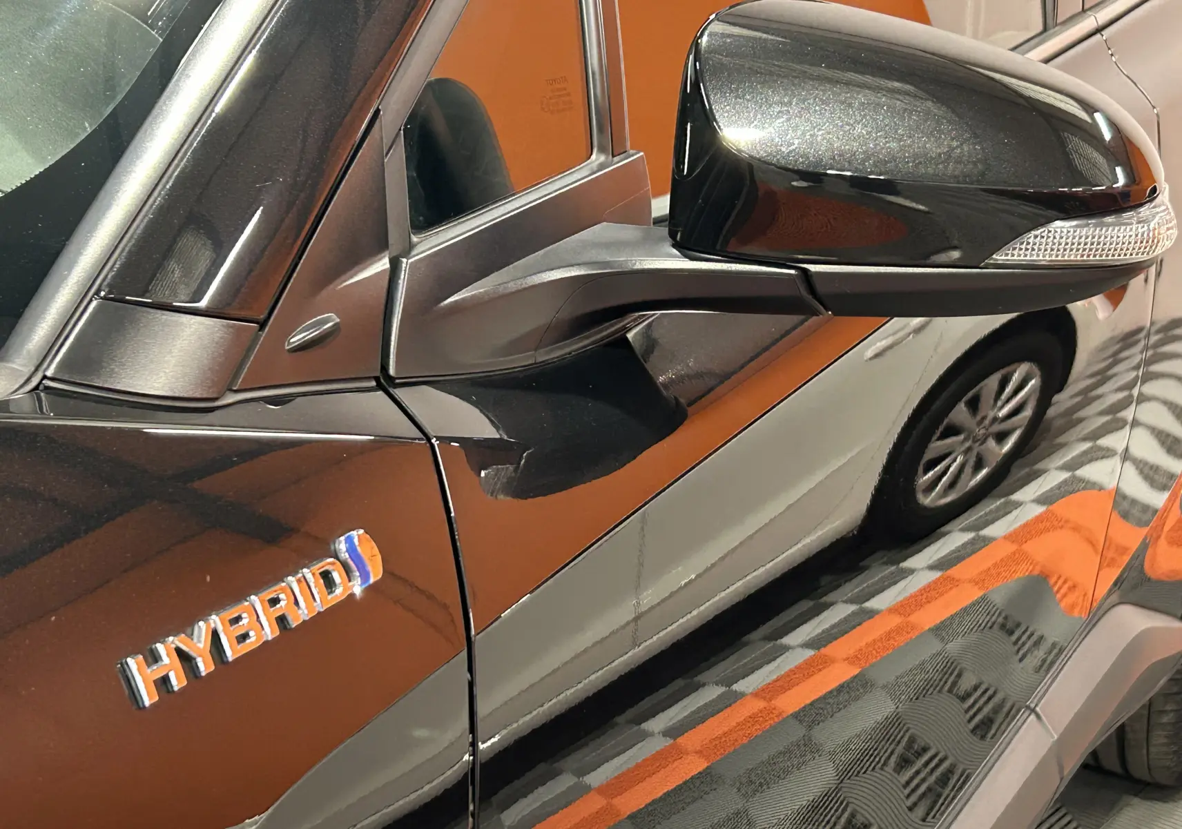 Détail du rétroviseur côté gauche et logo Hybrid sur la porte d’un Toyota C-HR Hybride noir métal.