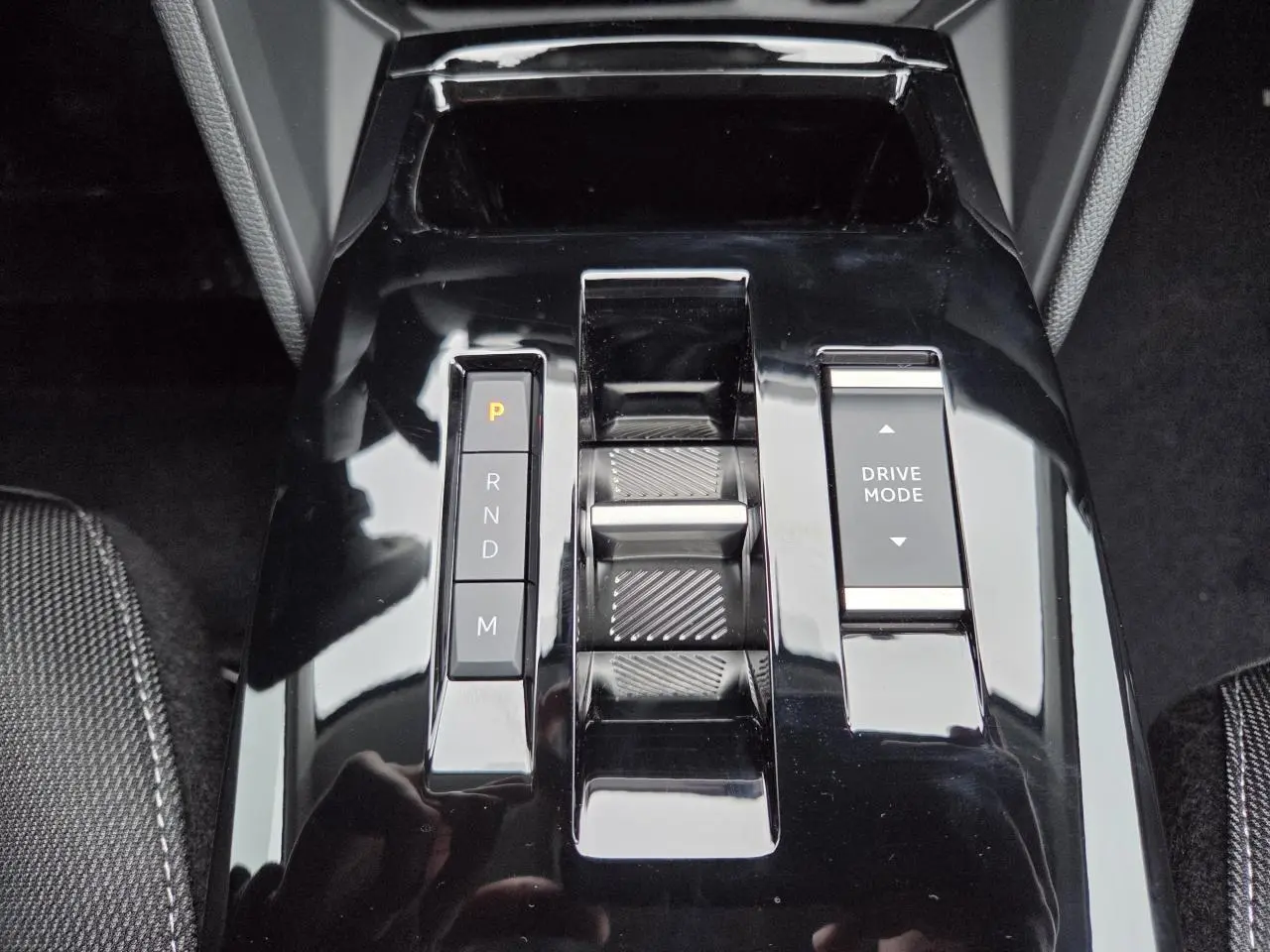 Gros plan sur la console centrale noire brillante de la Citroën C4 hybride 2025 avec commandes de boîte auto et mode de conduite.