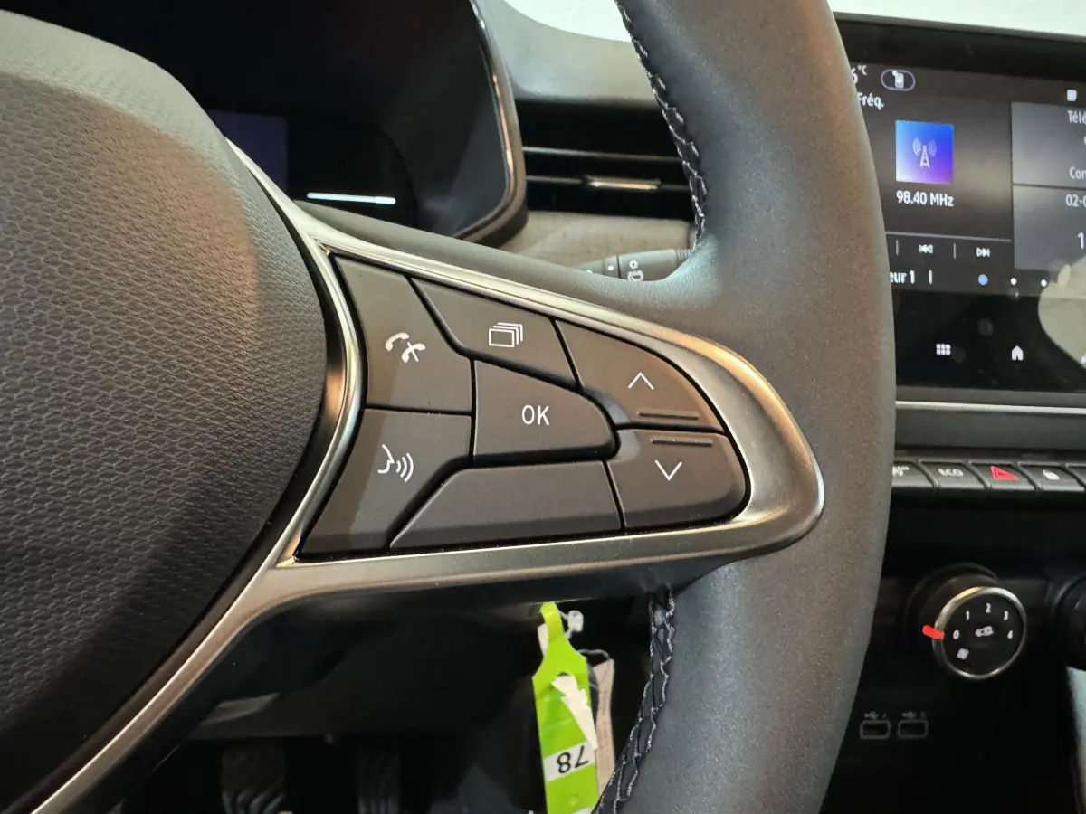 Gros plan sur les commandes multifonctions à droite du volant cuir de la Renault Clio gris clair, avec écran tactile en arrière-plan.