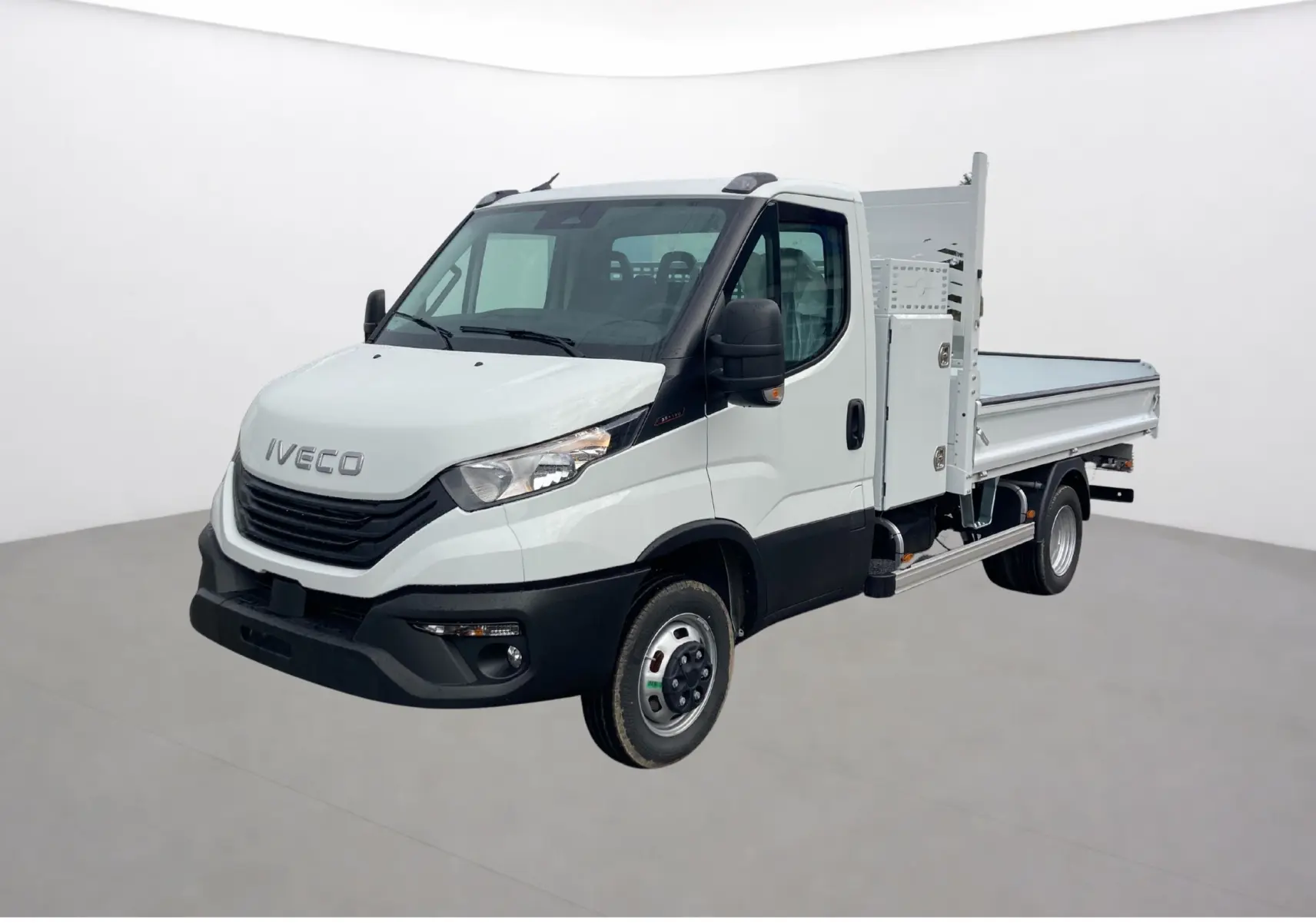 IVECO Daily blanc en 3/4 avant droit, avec benne acier et coffre latéral visible côté droit.