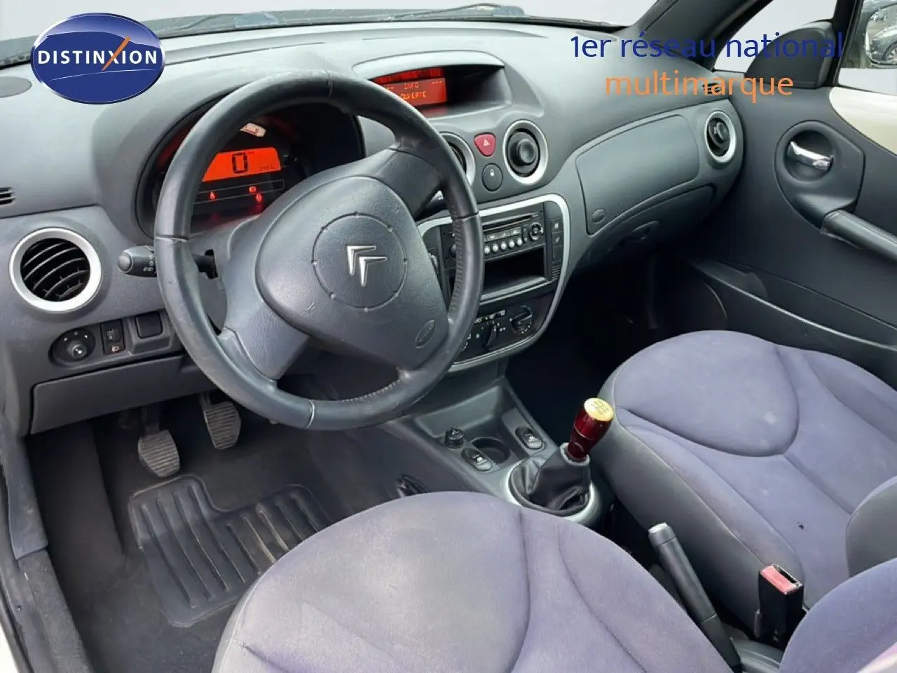 Vue intérieure côté conducteur de la Citroën C3 Pluriel 2007, volant cuir noir et sièges tissu gris bleu.