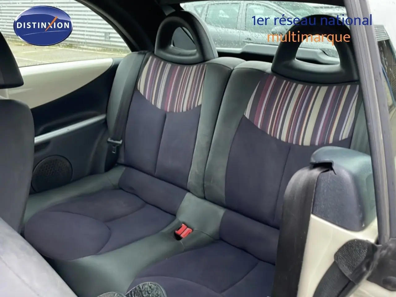 Vue intérieure arrière montrant les sièges arrière en tissu noir et beige avec motifs rayés sur une Citroën C3 Pluriel ivoire.