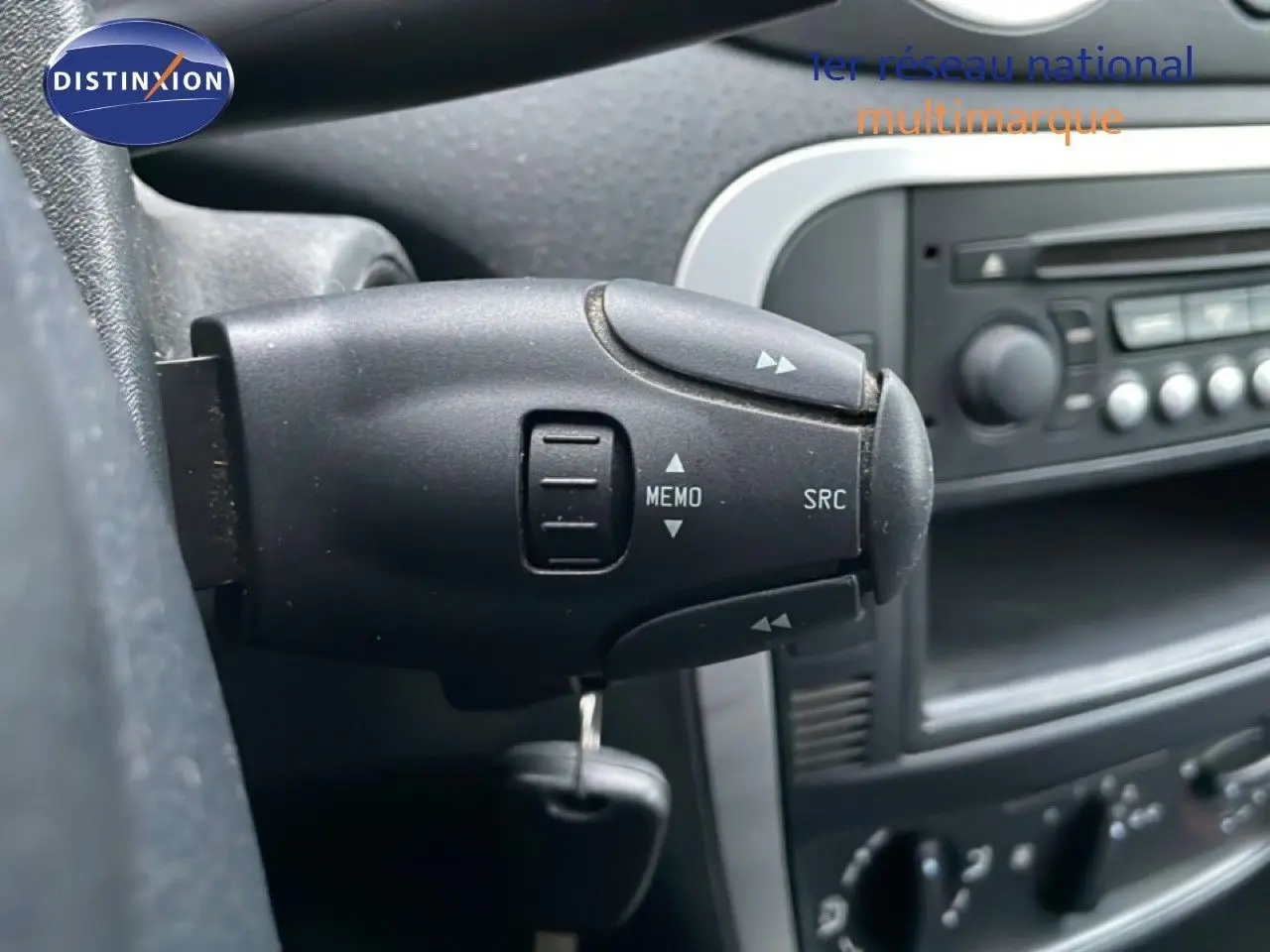 Gros plan sur la commande au volant côté gauche d’une Citroën C3 Pluriel ivoire, tableau de bord en arrière-plan.