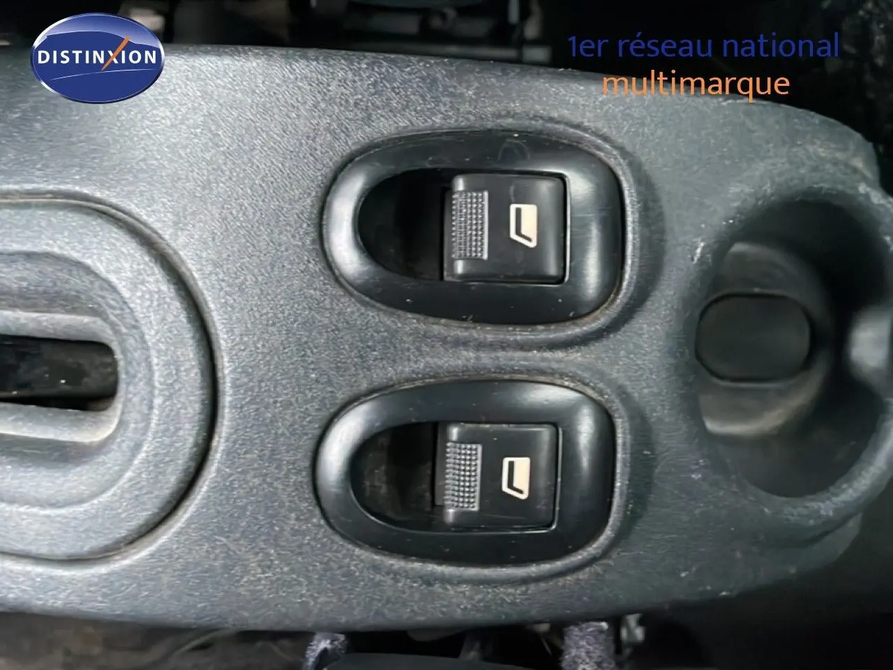Gros plan sur les commandes électriques des vitres avant dans l’habitacle d’une Citroën C3 Pluriel ivoire de 2007.